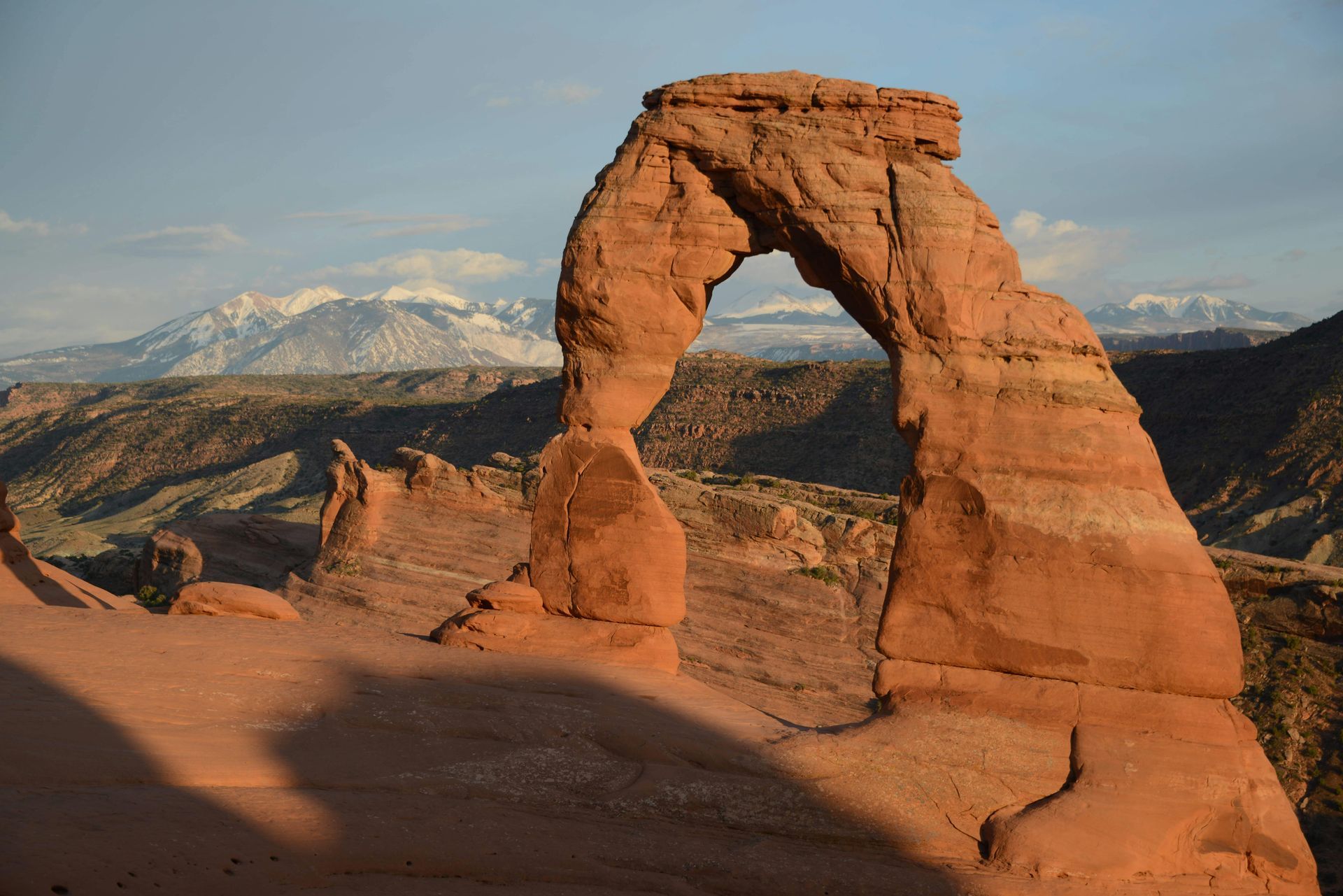 The Delicate Arch is in the middle of a desert with mountains in the background at Arches National Park in Utah.