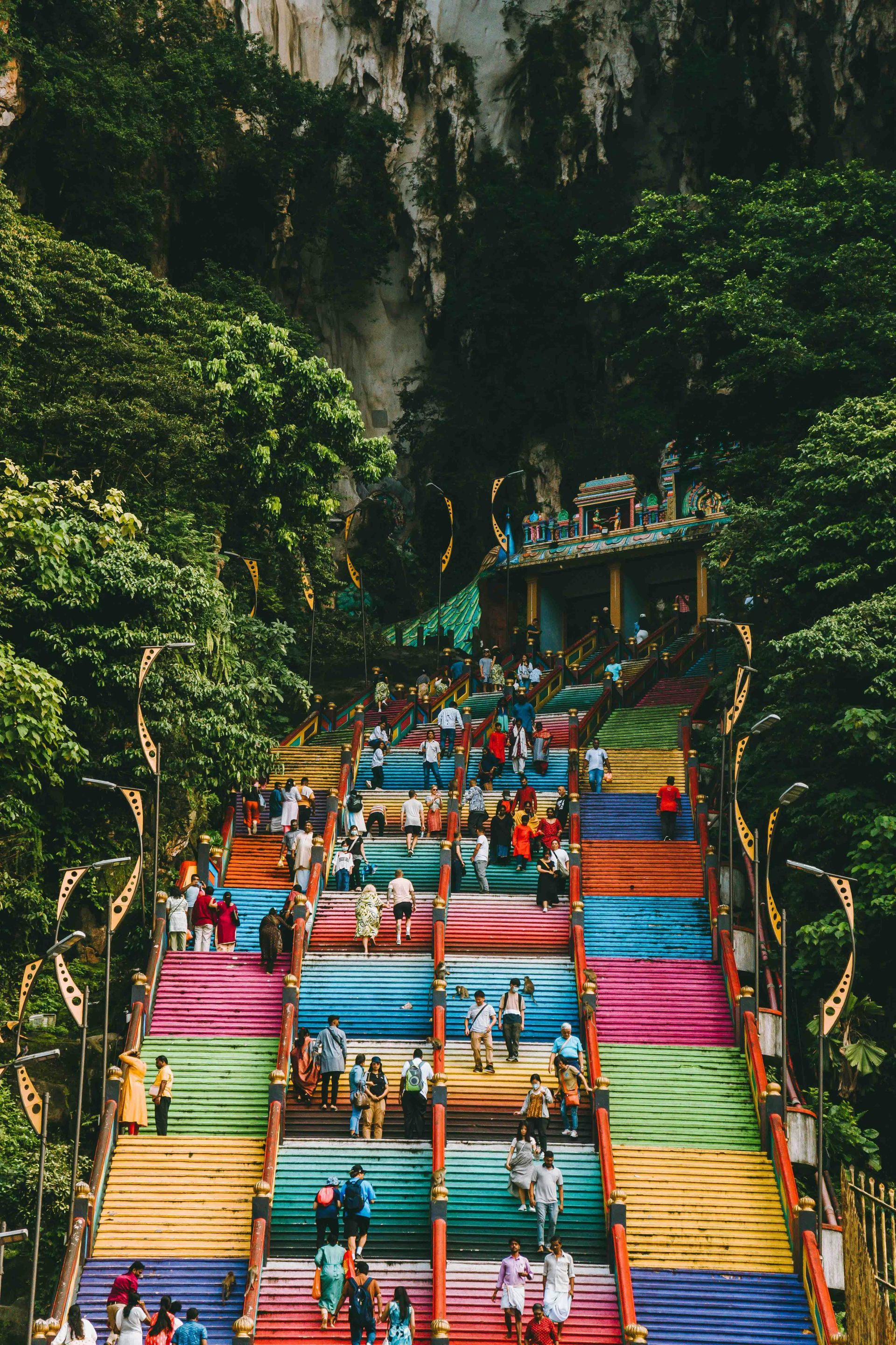 A group of people are walking down a set of colorful stairs at the Batu Caves in Malaysia.