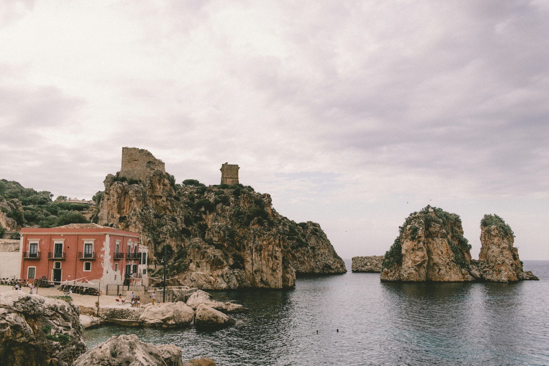 A castle on top of a rocky hill overlooking a body of water in Sicily, Italy.