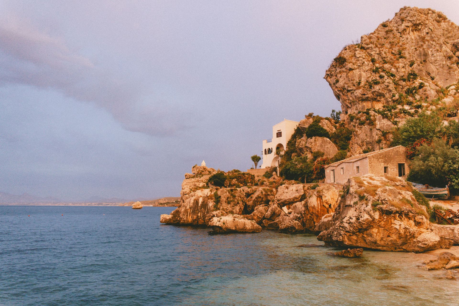 A house sits on a rocky cliff overlooking the ocean in Sicily, Italy.