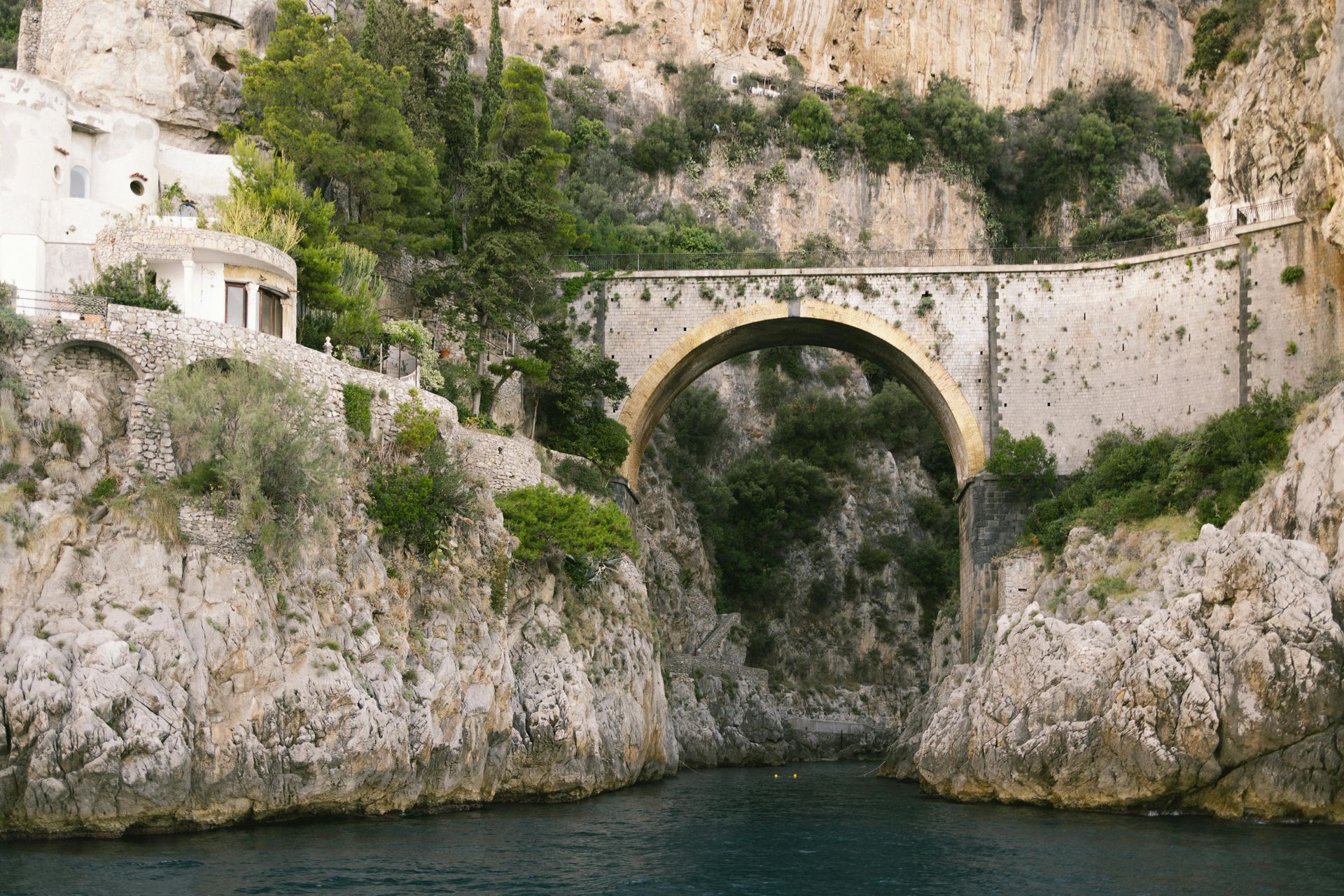 A bridge over a body of water between two rocky cliffs in the Amalfi Coast, Italy.