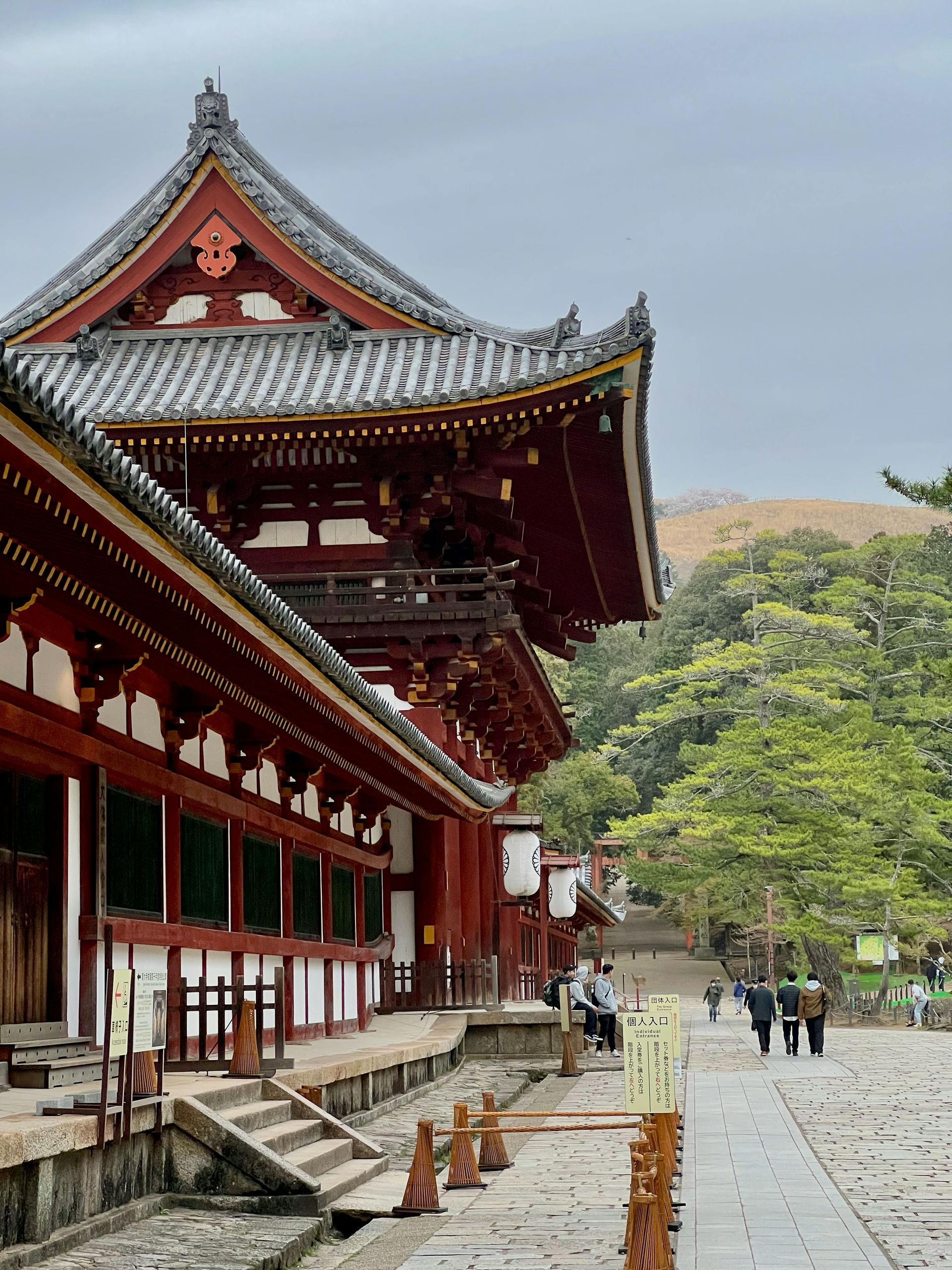 A group of people are walking in front of a large building with a red roof in Japan. 