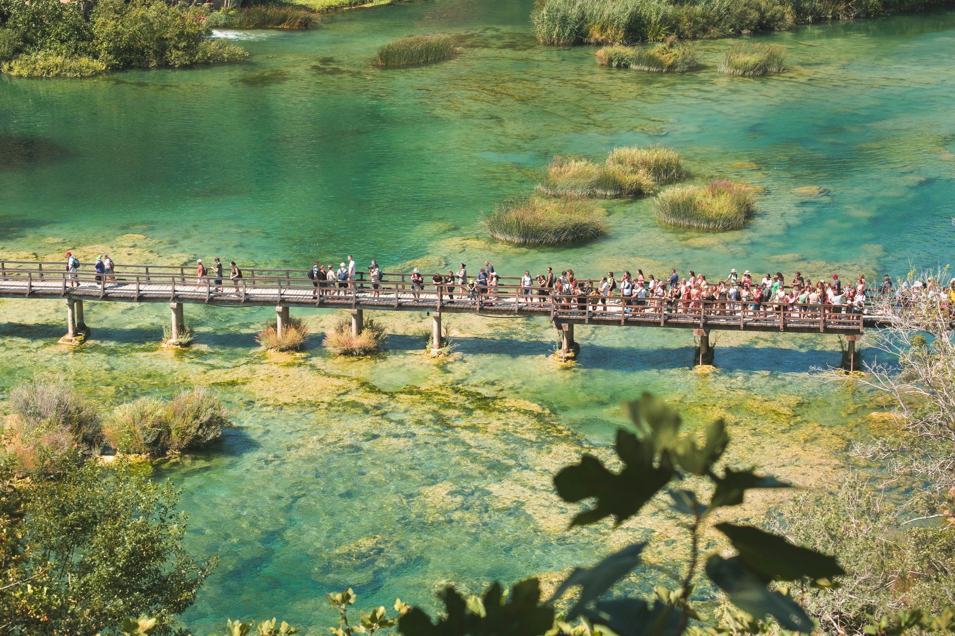 A group of people are walking across a bridge over a lake at Krka National Park in Croatia. 