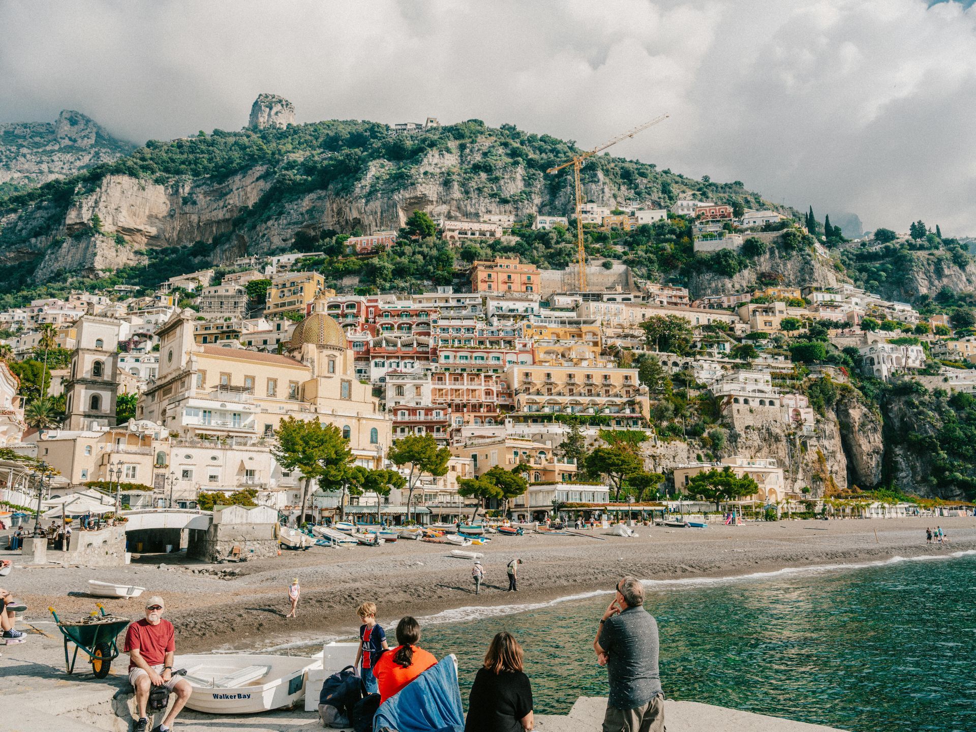 A group of people standing on a pier next to a body of water with the Amalfi Coast in the background in Italy.