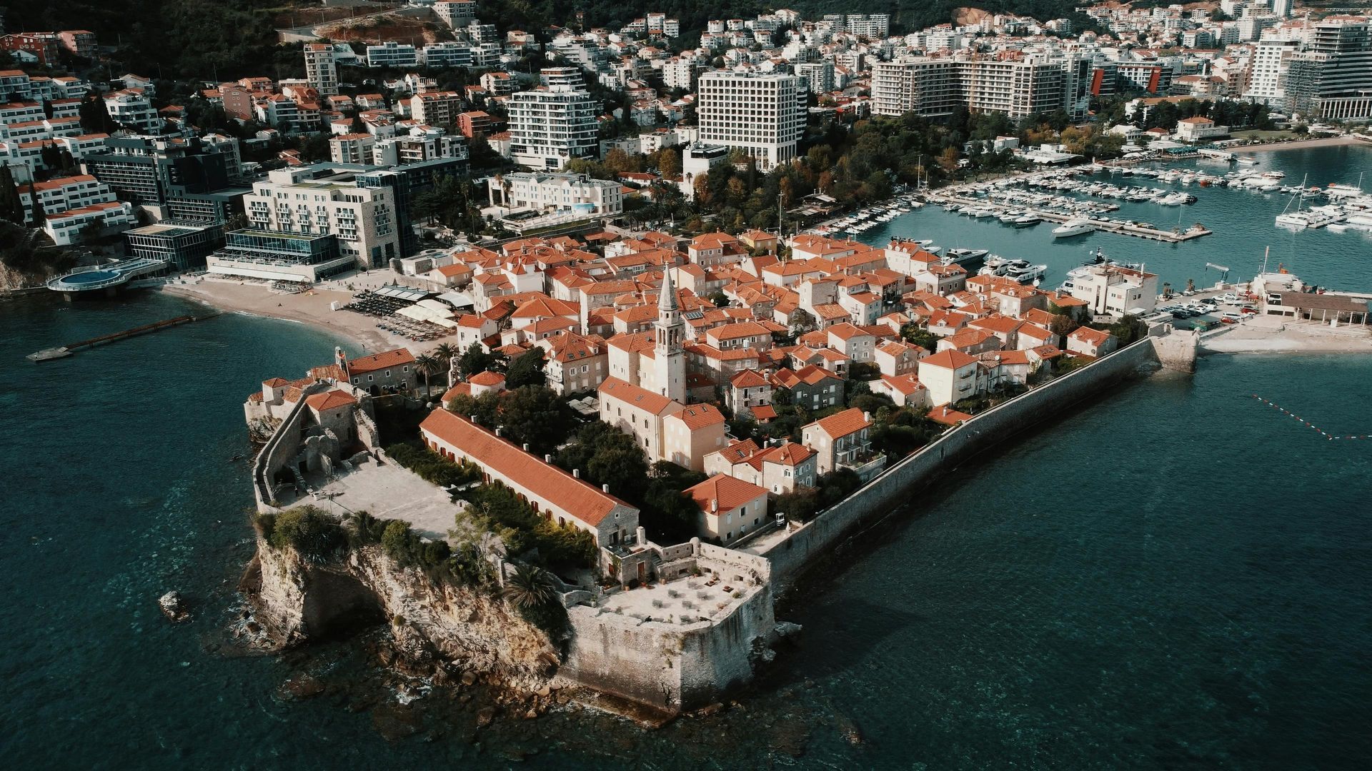 An aerial view of a small island in the middle of the ocean with a city in the background in Budva, Montenegro. 