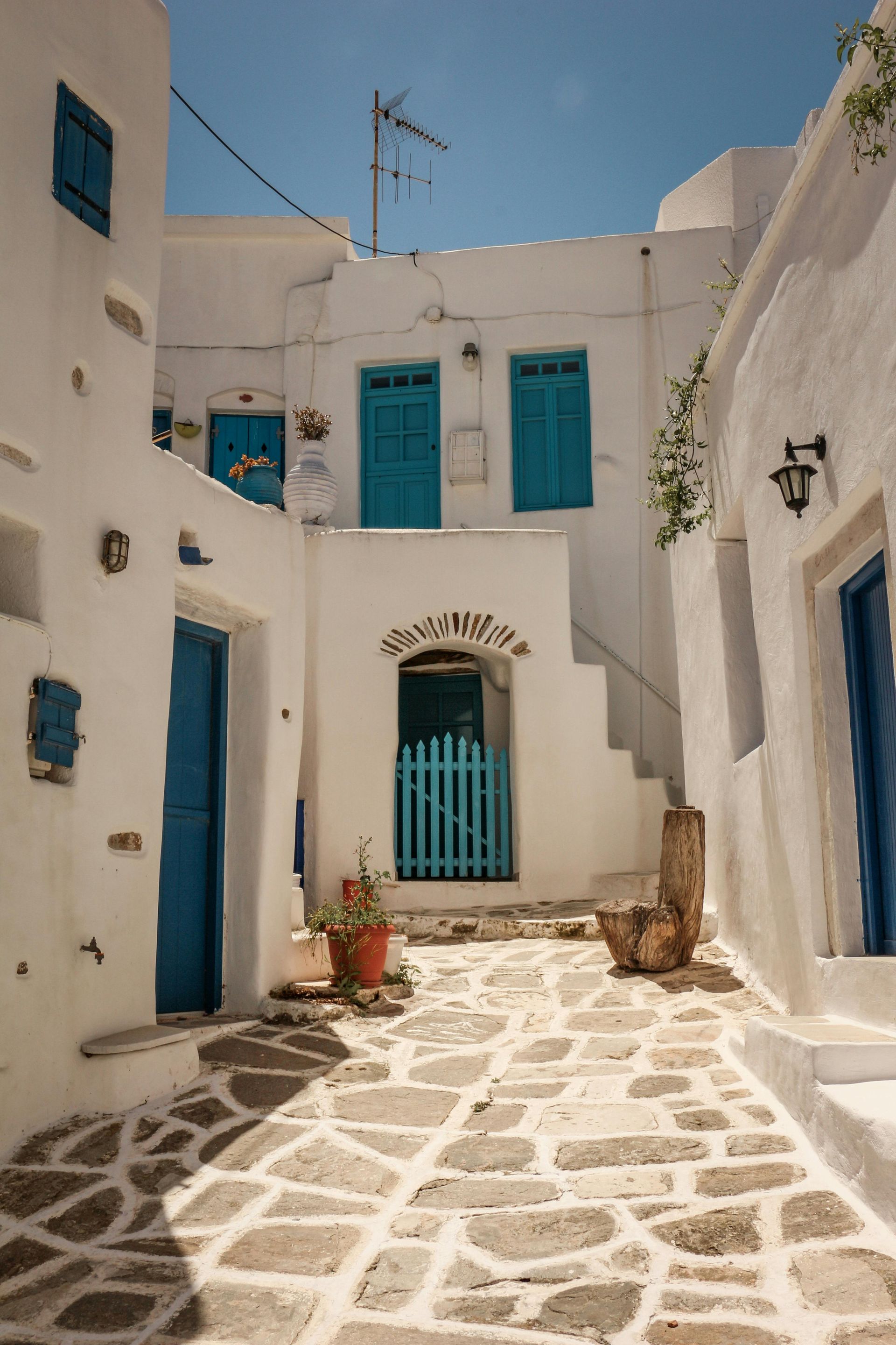 A narrow alleyway between two white buildings with blue doors in Paros, Greece.