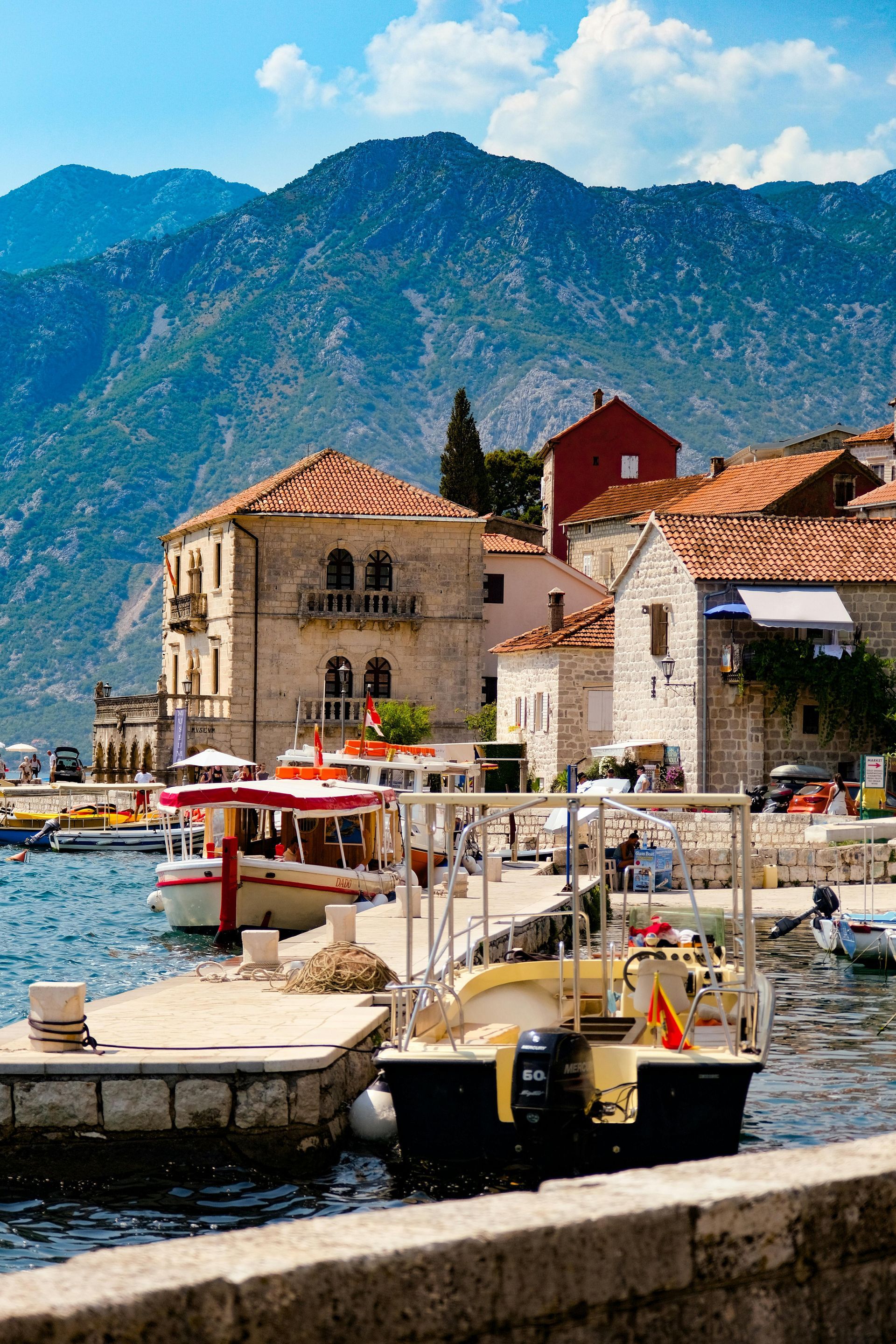 A group of boats are docked in a harbor with mountains in the background in Montenegro.