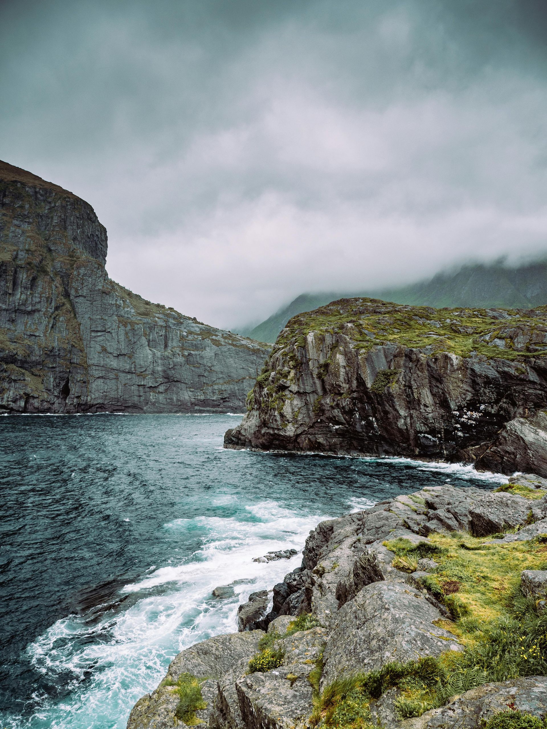 A cliff overlooking a body of water with mountains in the background in Iceland.