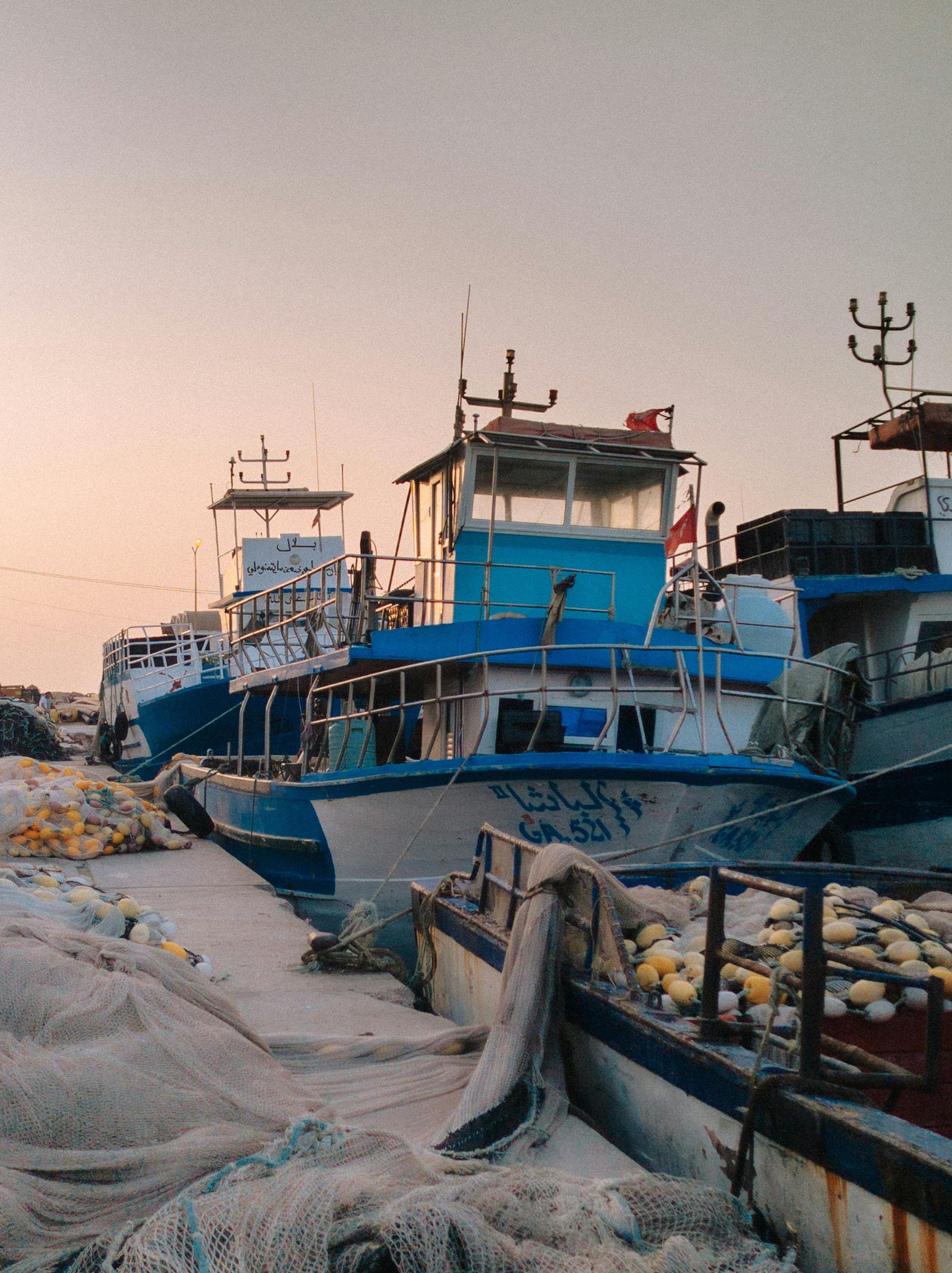 A row of boats are docked in a harbor and one of them has a graffiti on the side in Alaska.