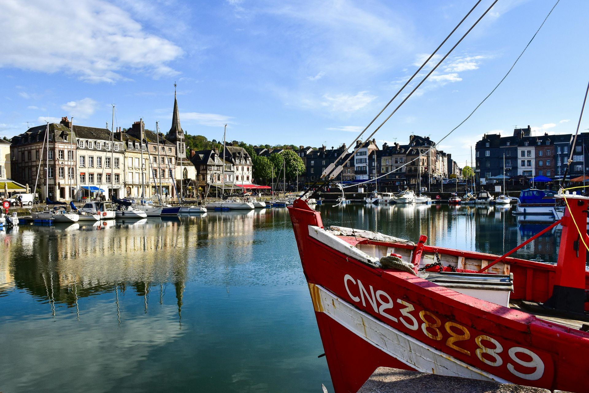 A red boat is docked in a harbor with buildings in the background in northern france.