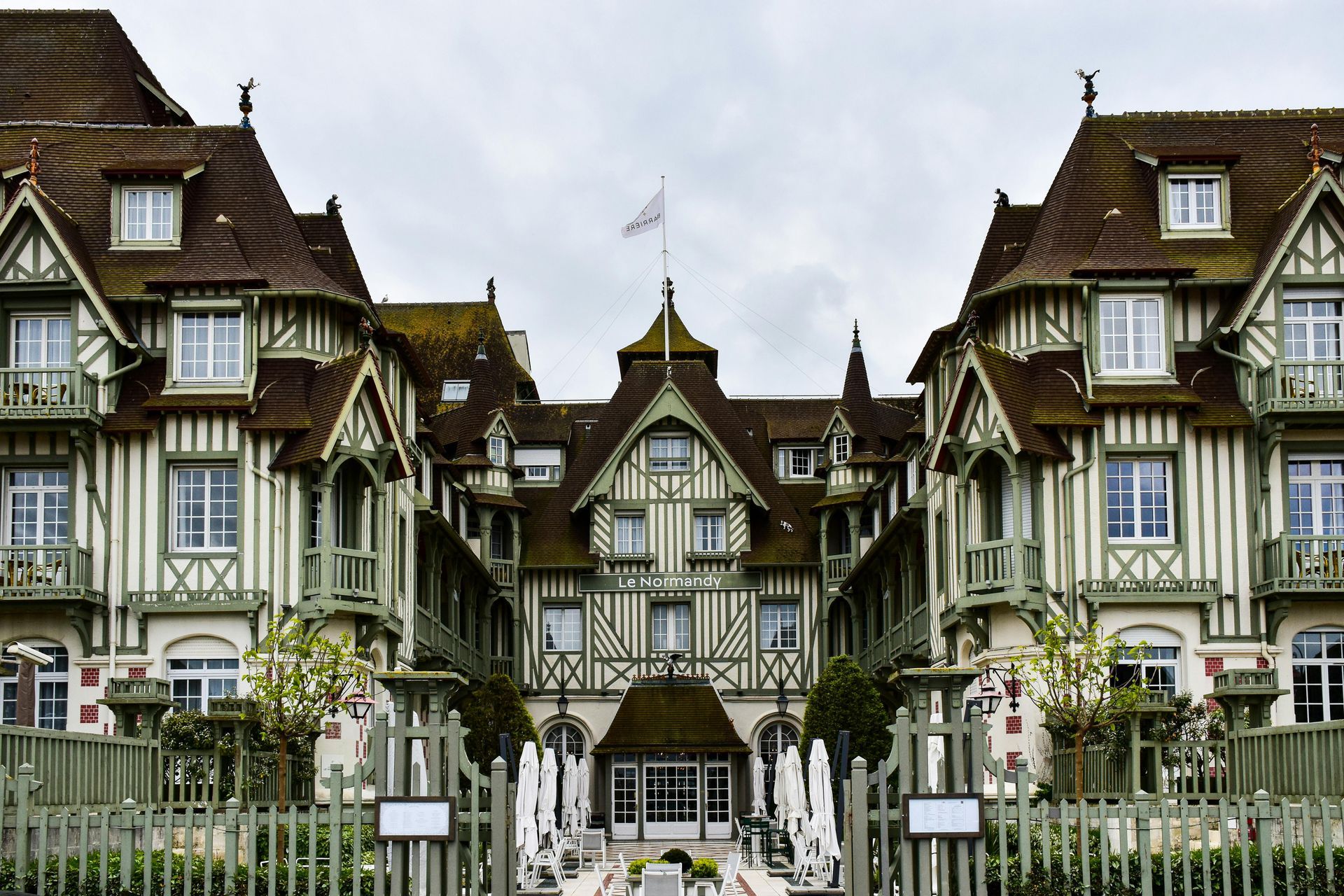 A large building with a flag on top of it is surrounded by a fence in northern France. 