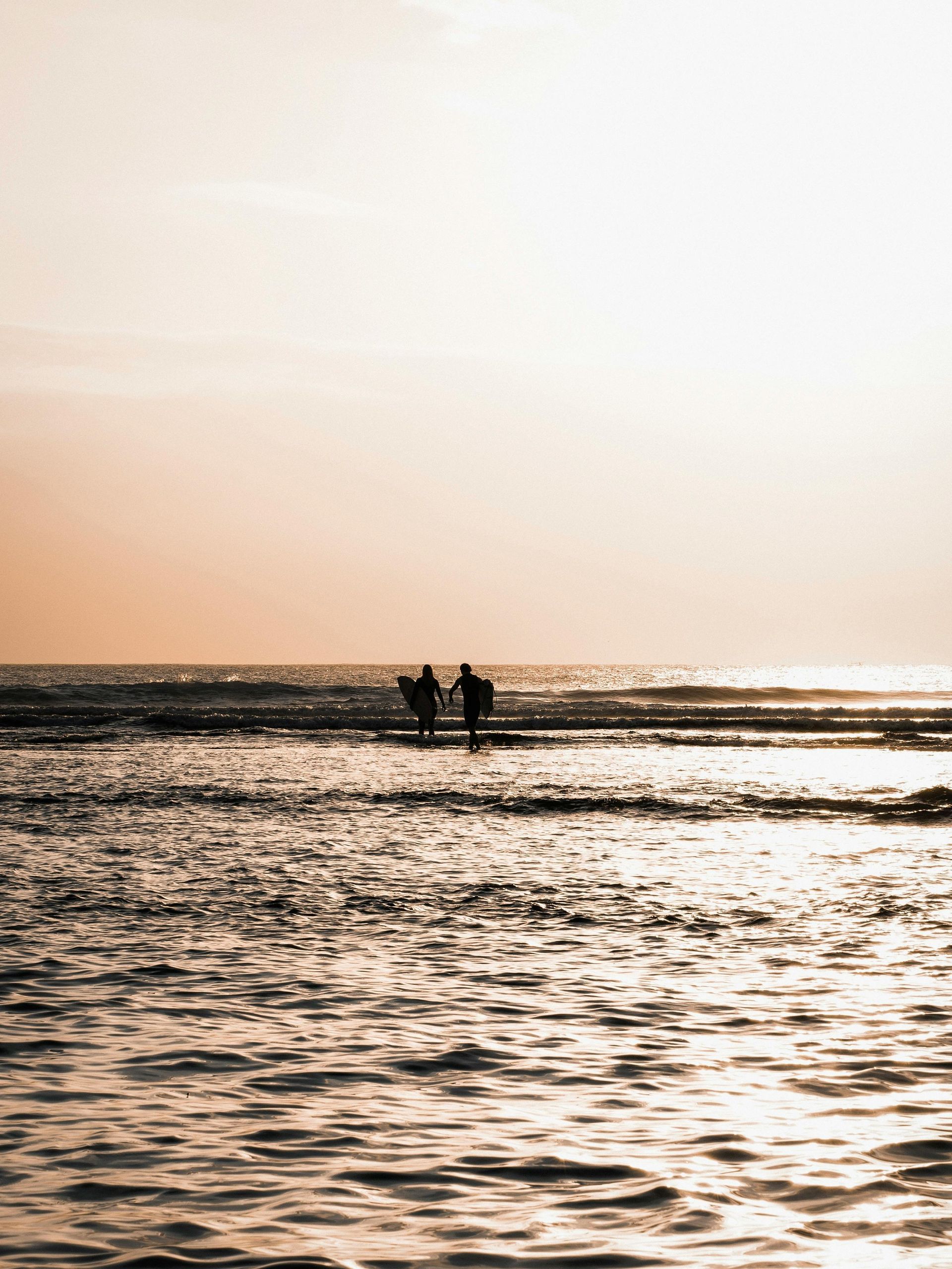 Two people are walking on a pier overlooking the ocean at sunset.