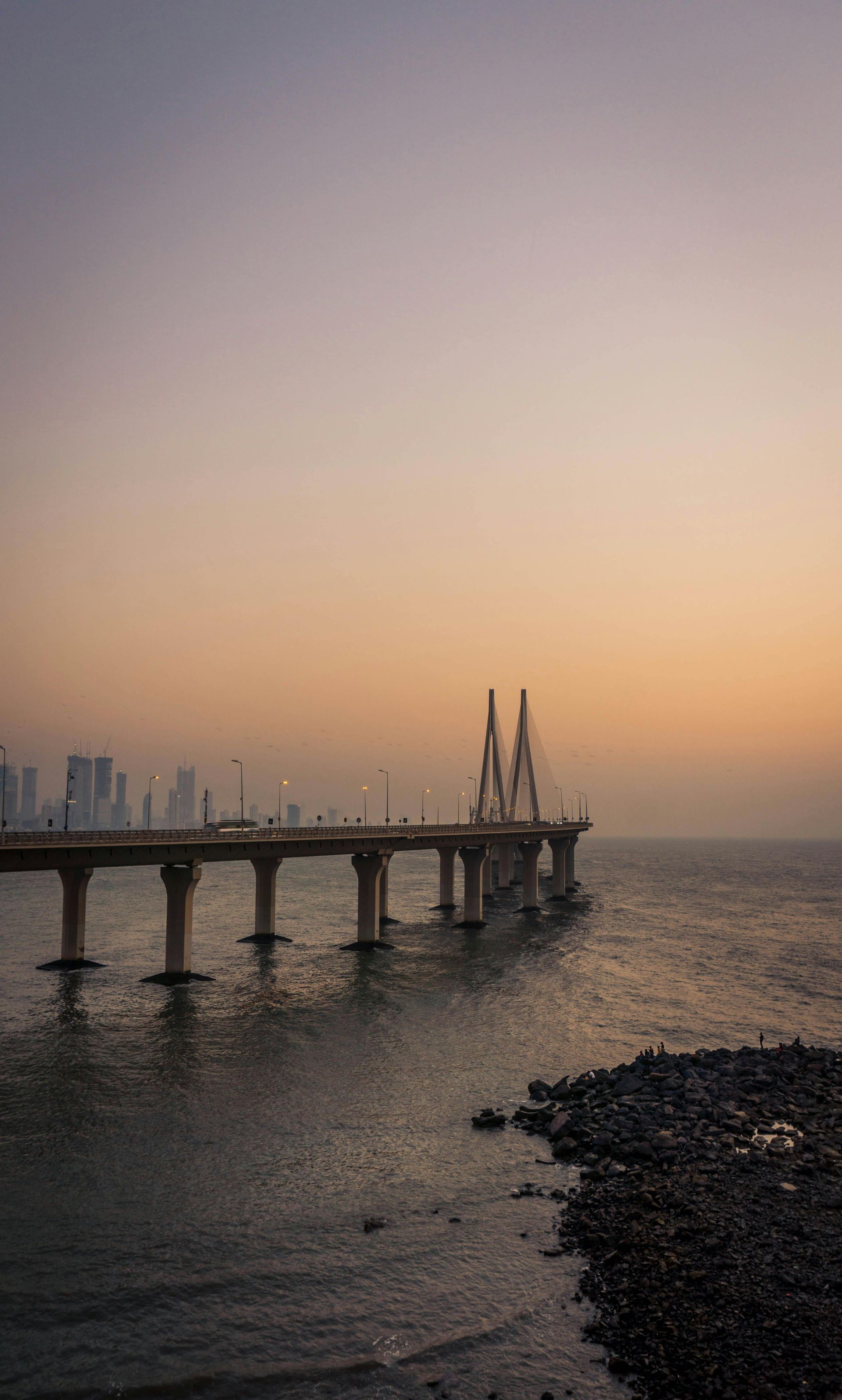 A bridge over a body of water at sunset with a city in the background.