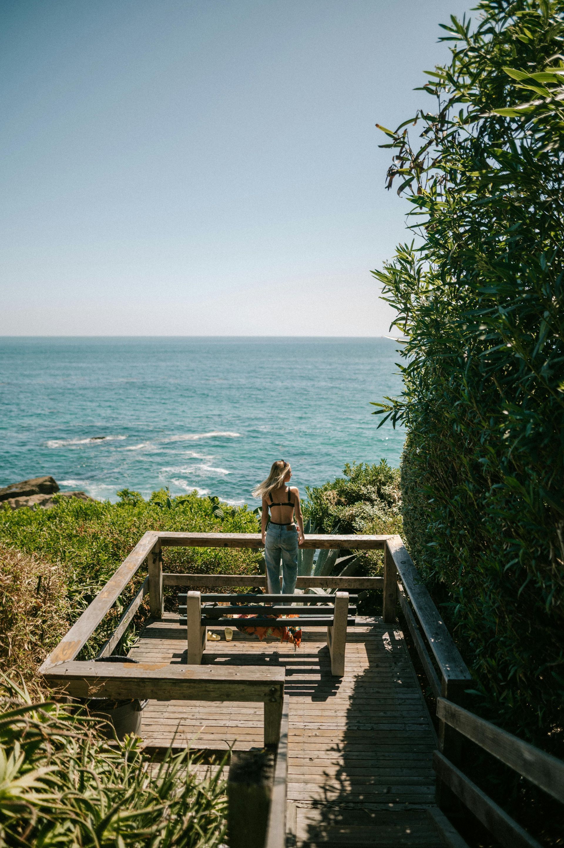 A woman is standing on a wooden deck overlooking the ocean.