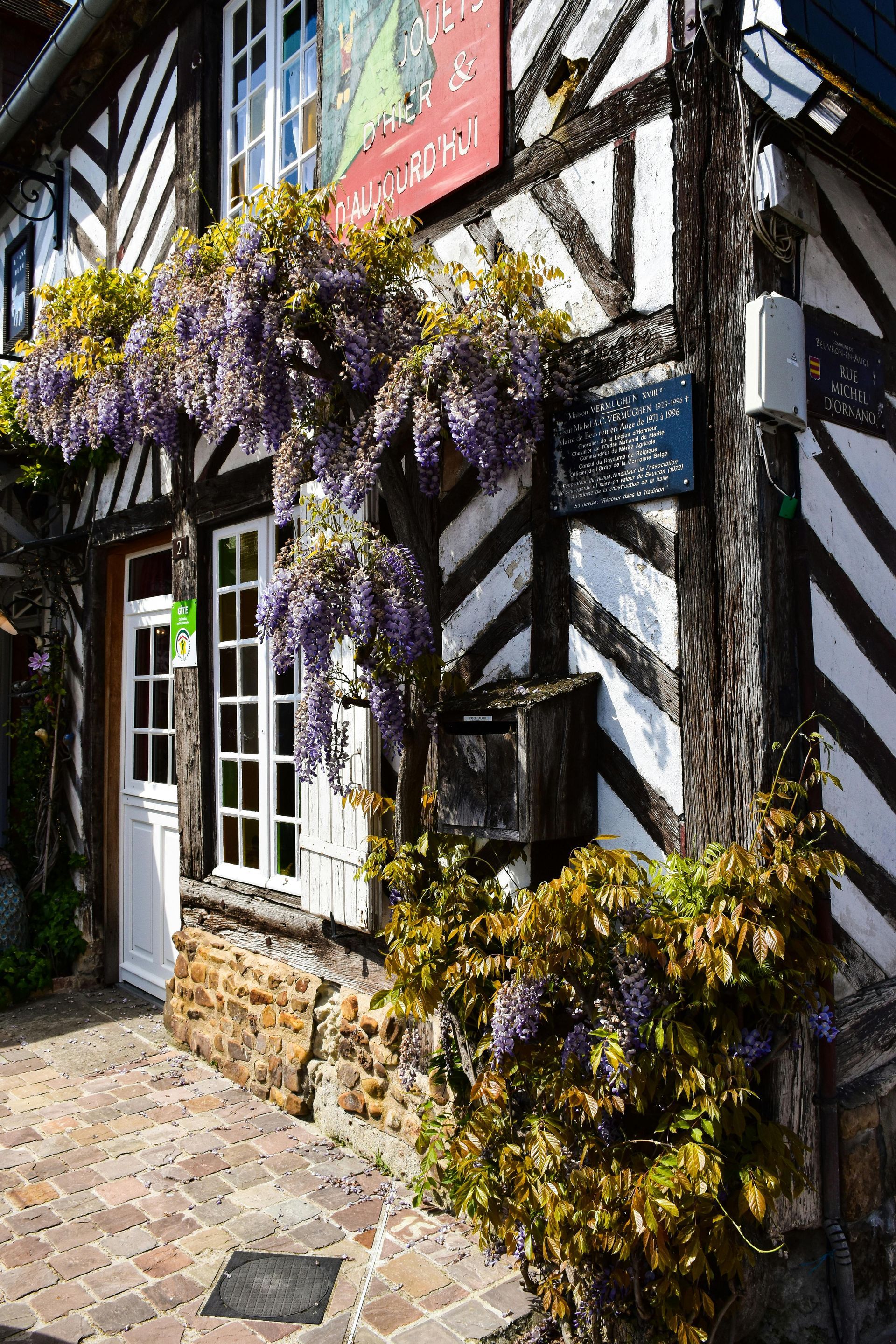 A black and white building with purple flowers on the side of it in northern france.