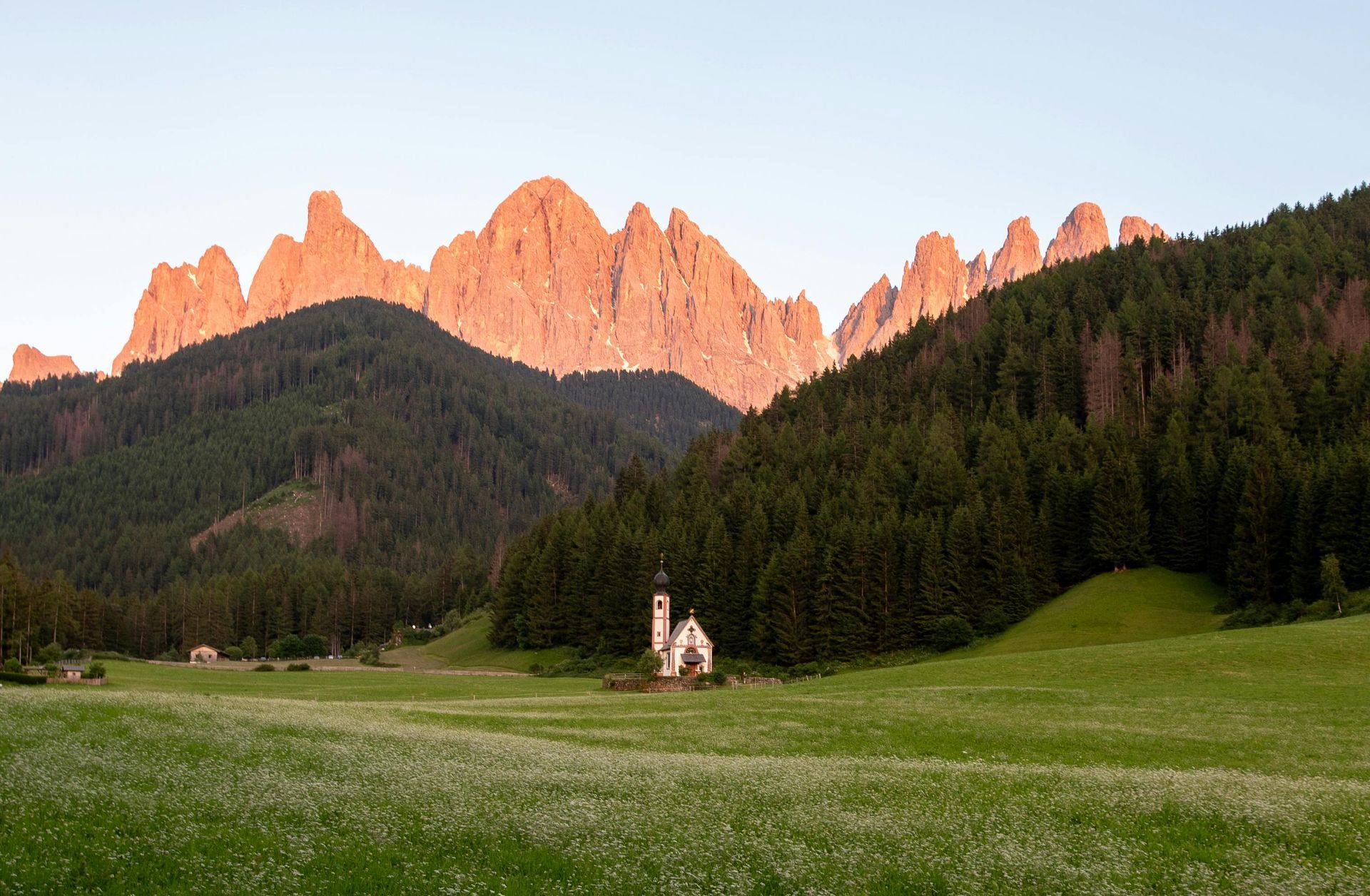 A church in the middle of a field with The Dolomites in the background in Italy.