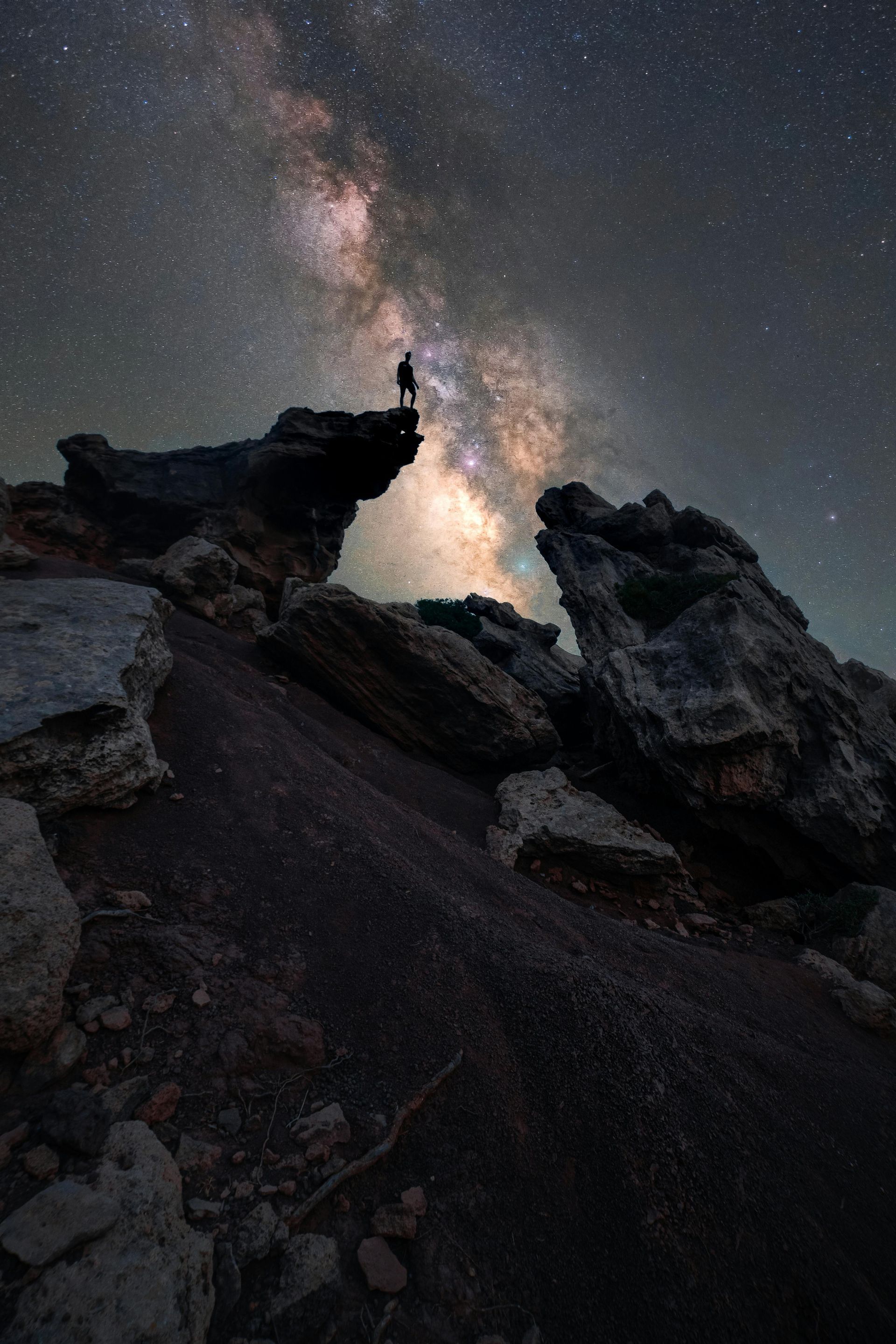 A person is standing on top of a rocky cliff under a starry sky.