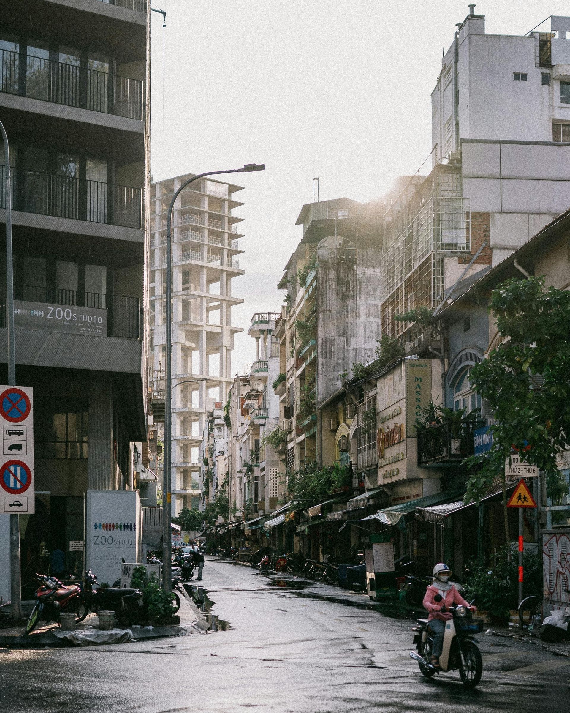 A man is riding a motorcycle down a city street next to a no parking sign in Japan.