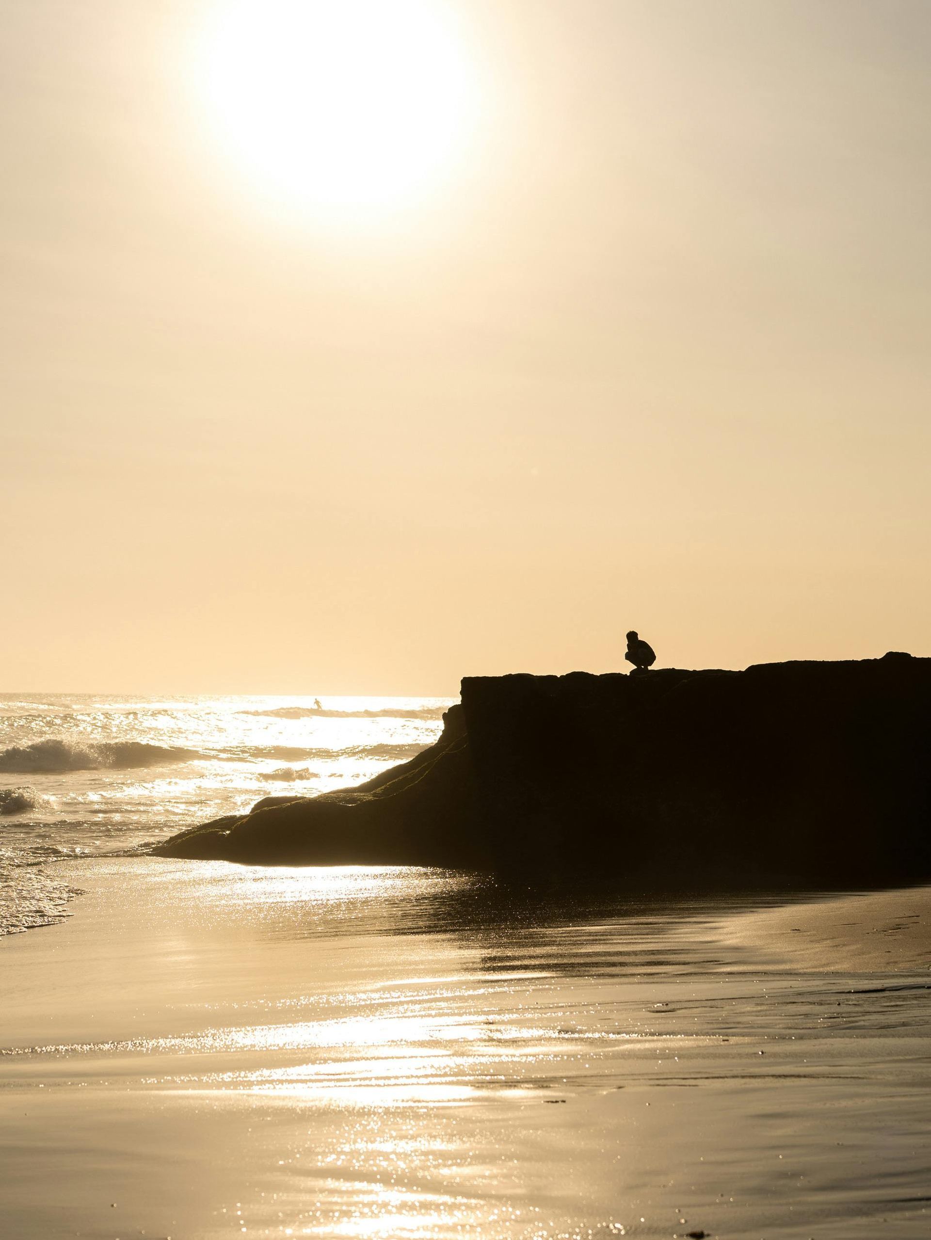 A person is sitting on a pier overlooking the ocean at sunset.