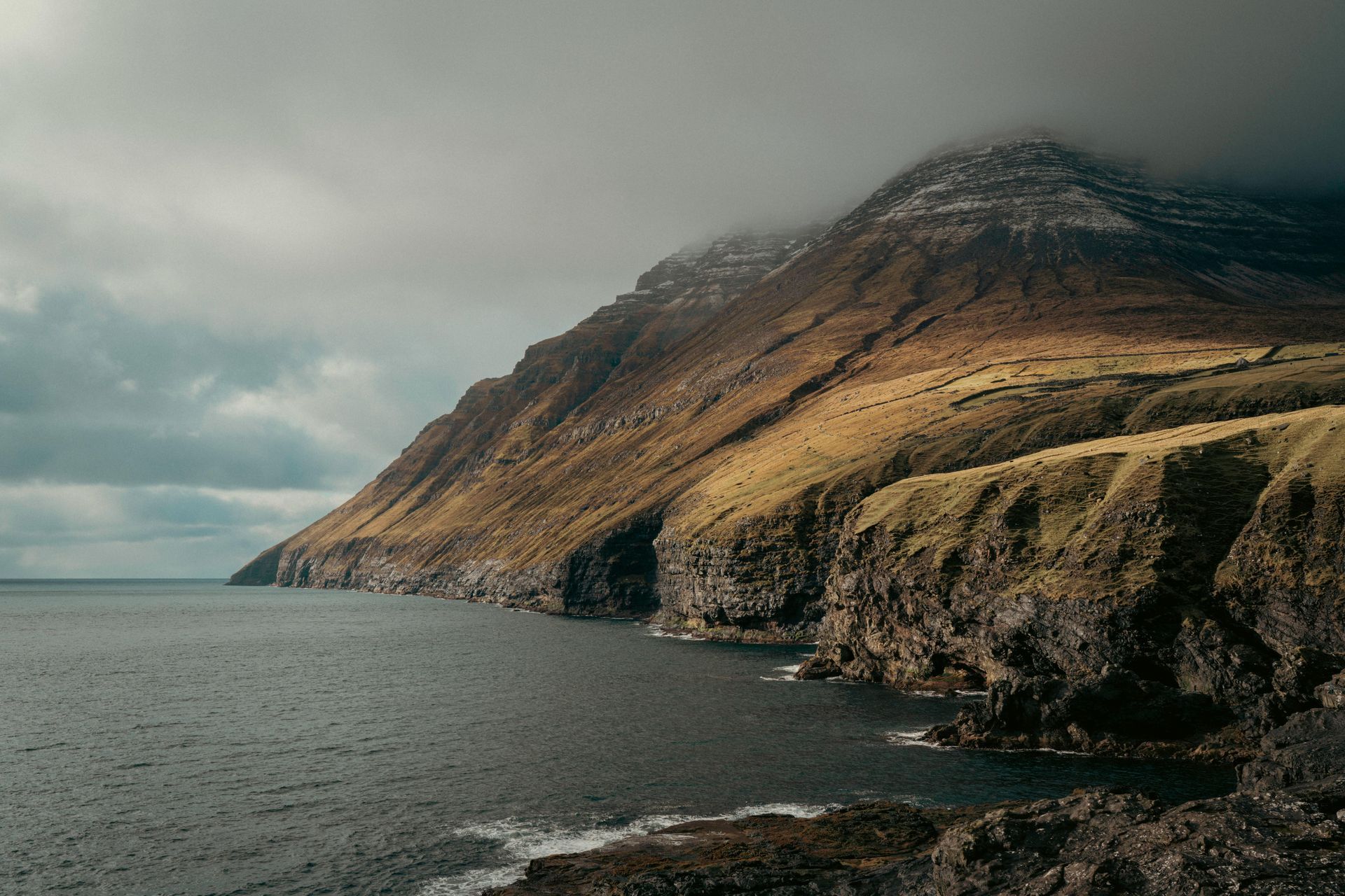 There is a waterfall on the side of a cliff next to the ocean on the Faroe Islands.