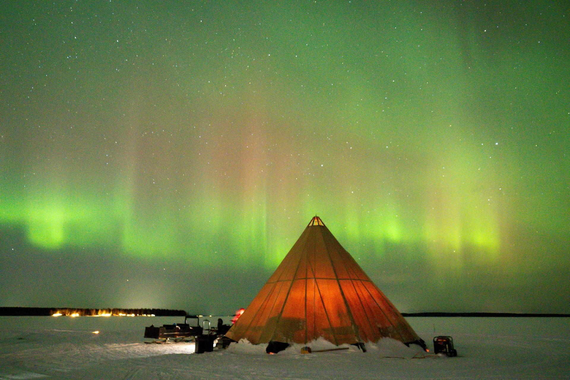 A teepee in the snow under the aurora borealis in Sweden.