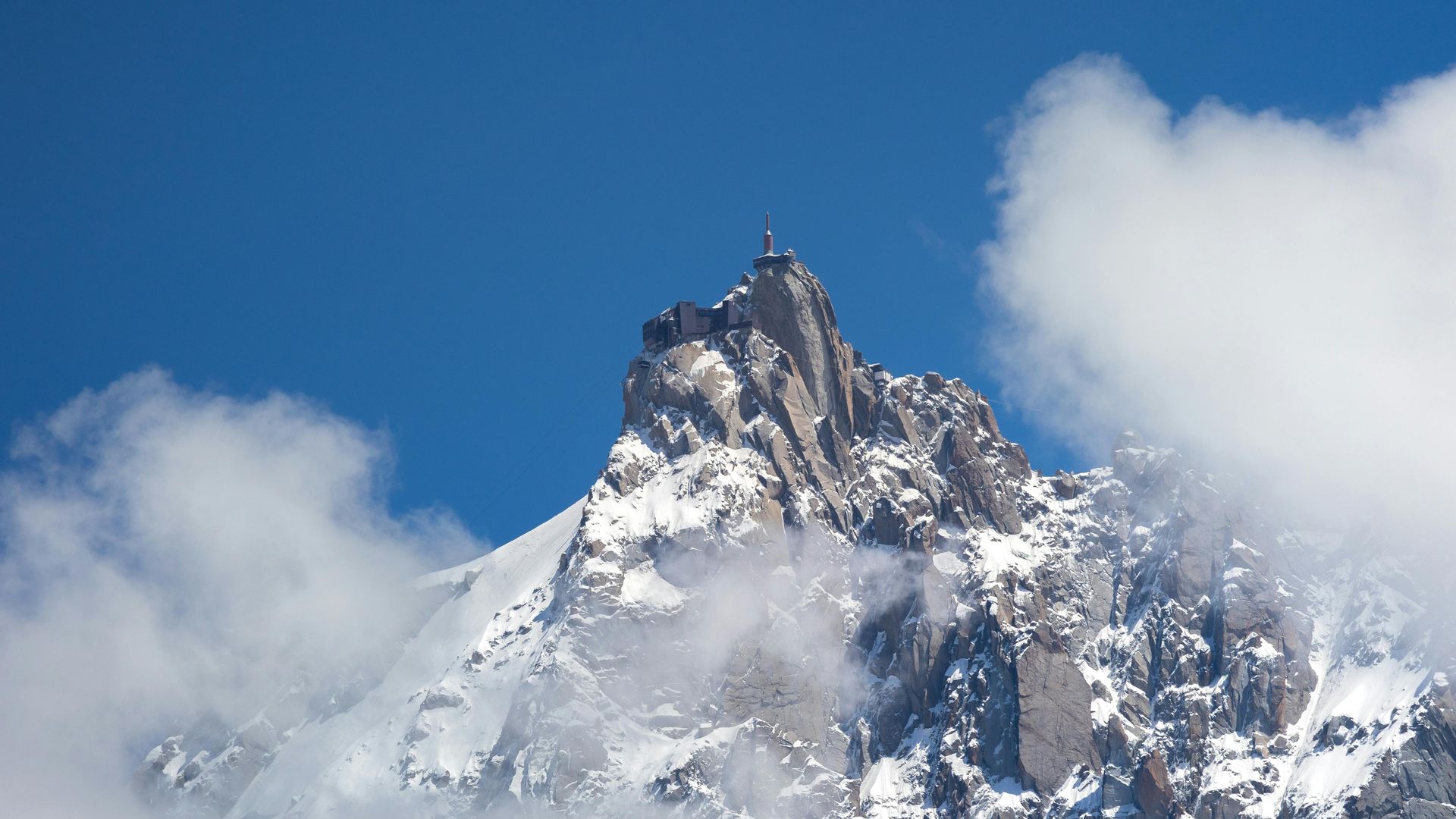 A snowy mountain covered in clouds with a blue sky in the background in Chamonix, France.