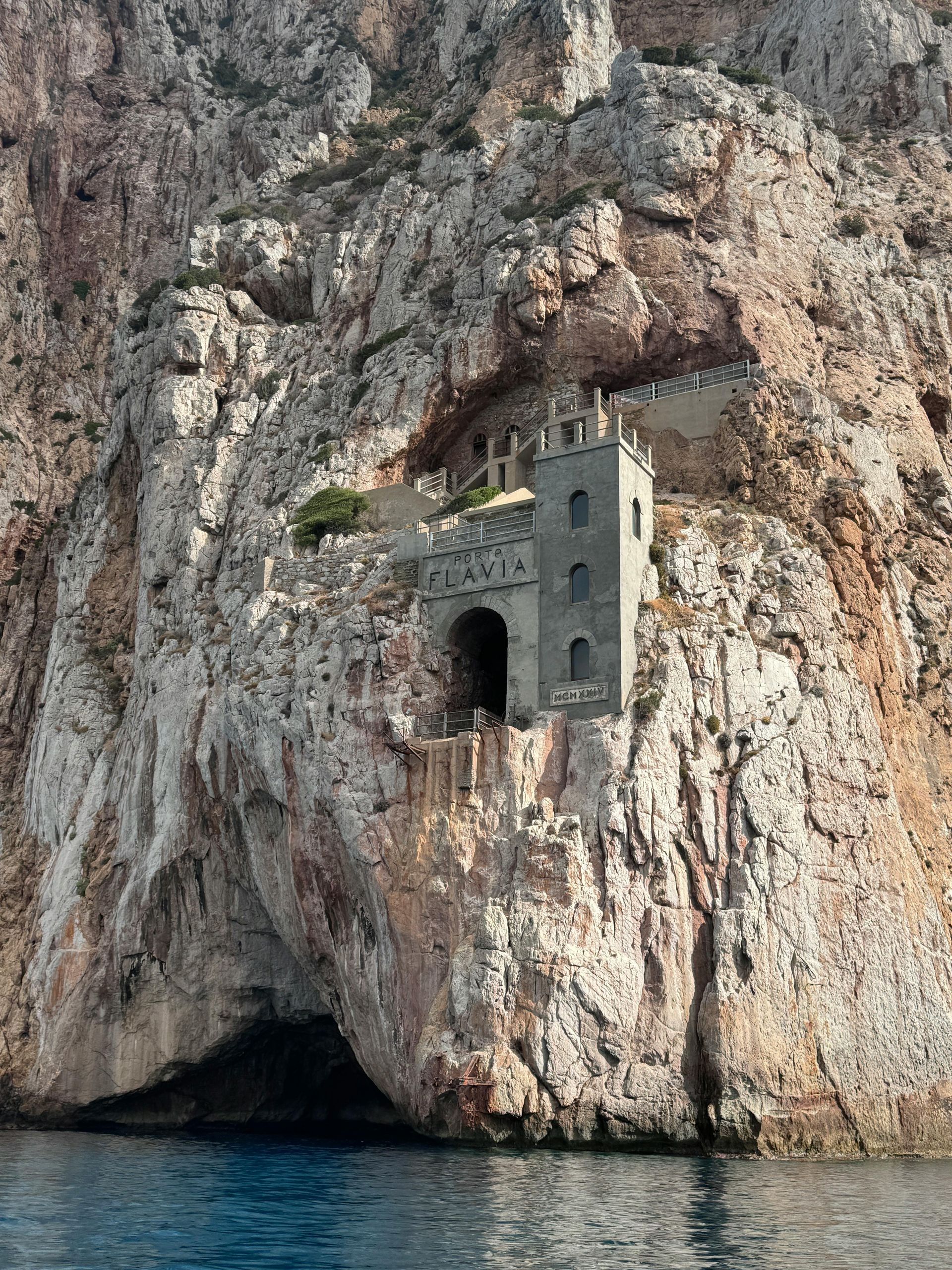 A building on top of a rocky cliff overlooking the ocean in Sardinia, Italy.