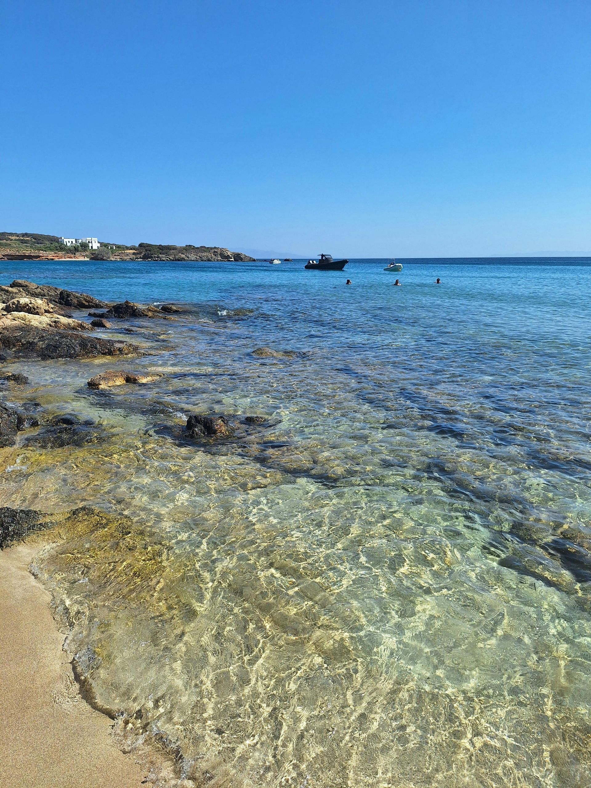 A boat is floating on the water near the shore of a beach in Paros, Greece.