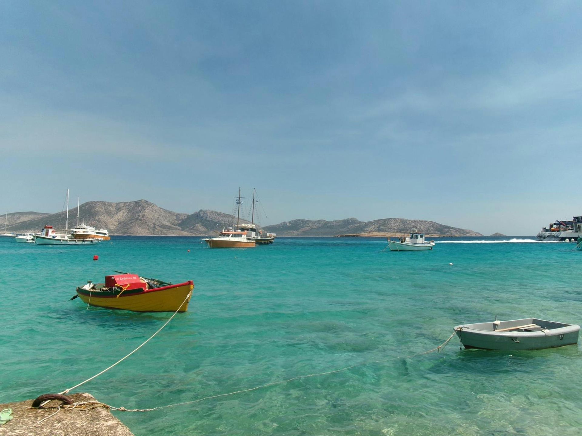 A group of boats are floating on top of a large body of water in Milos, Greece.