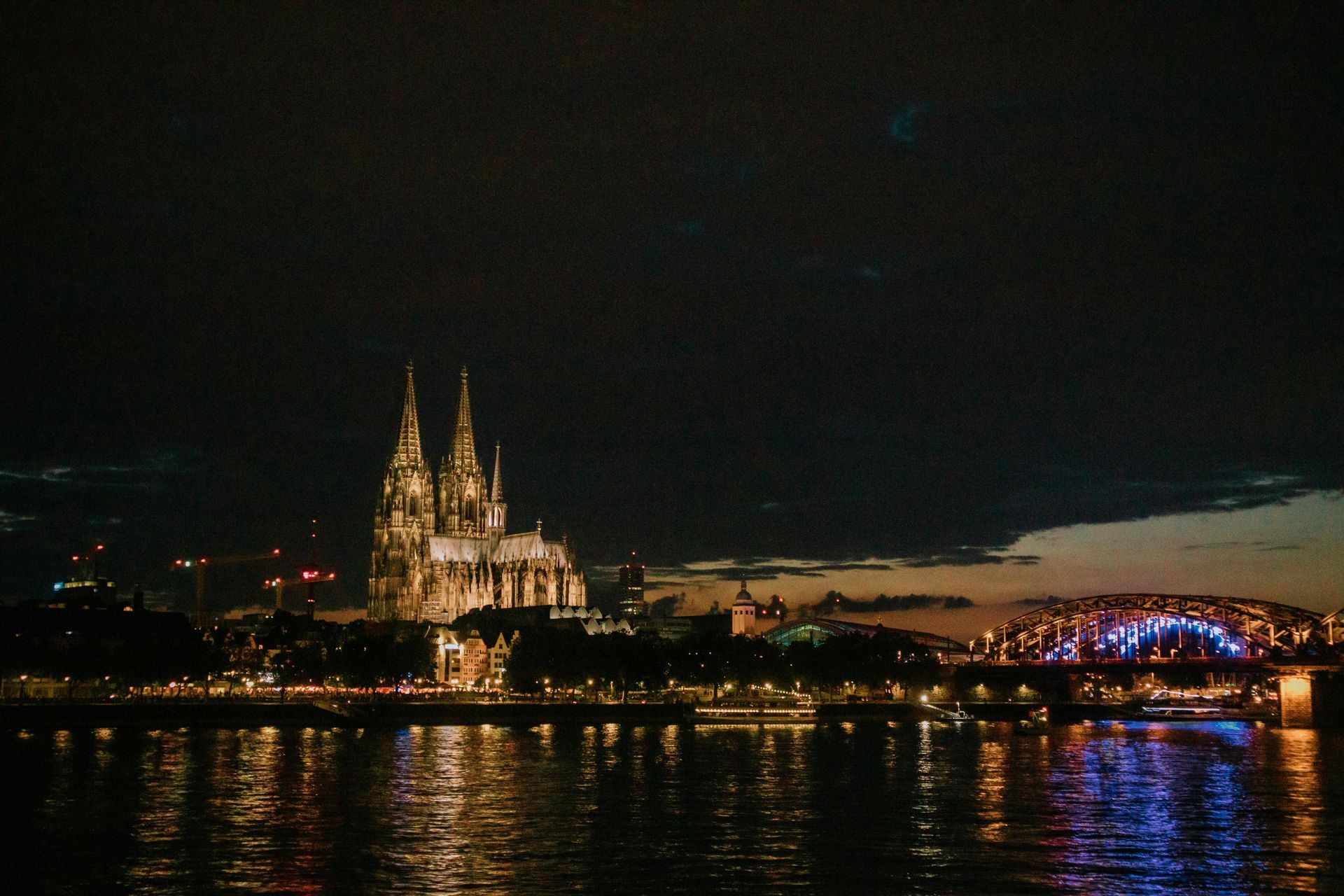 A large cathedral is lit up at night overlooking The Rhine River.