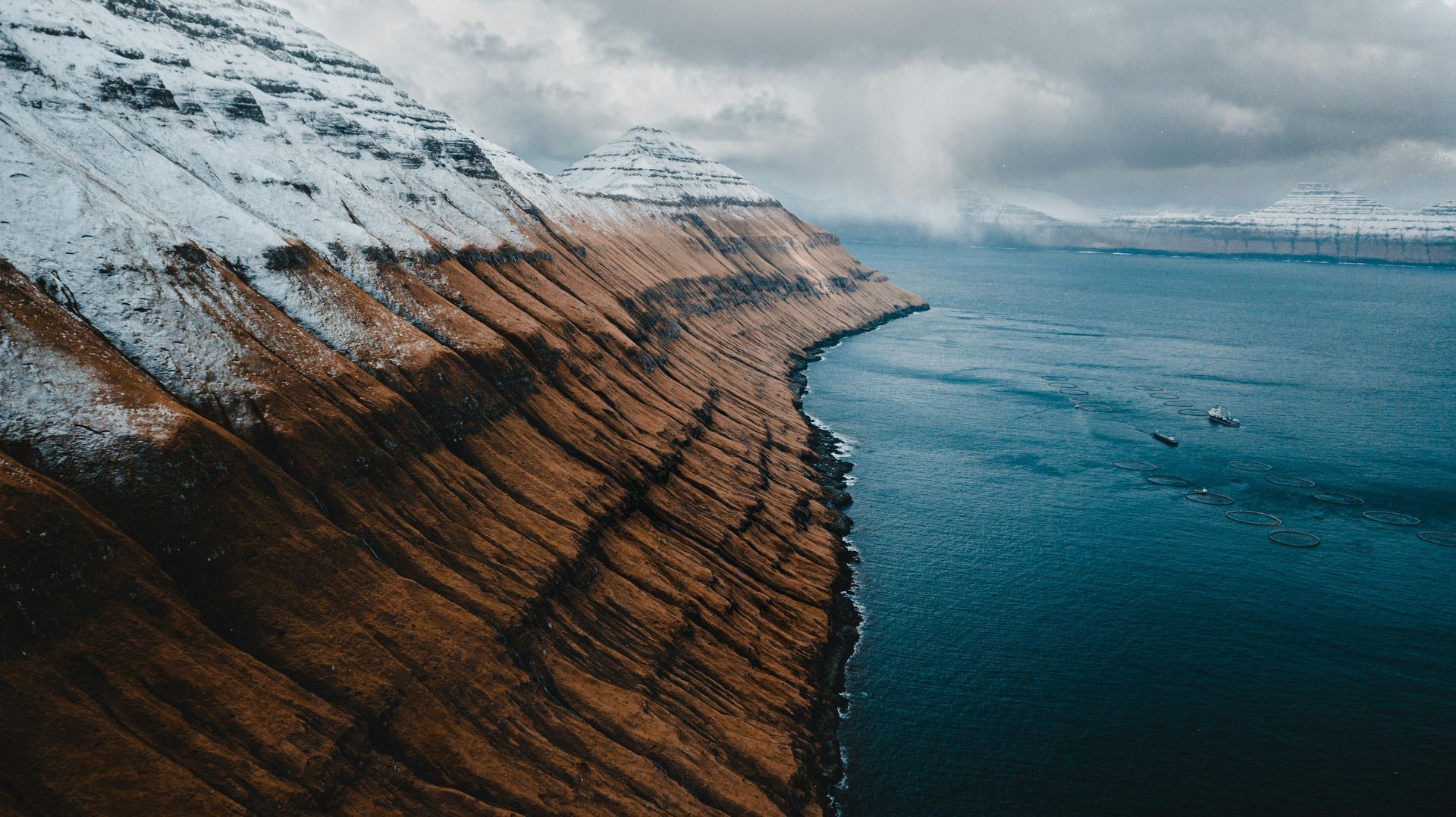 A cliff overlooking the ocean with a mountain in the background on the Faroe Islands.