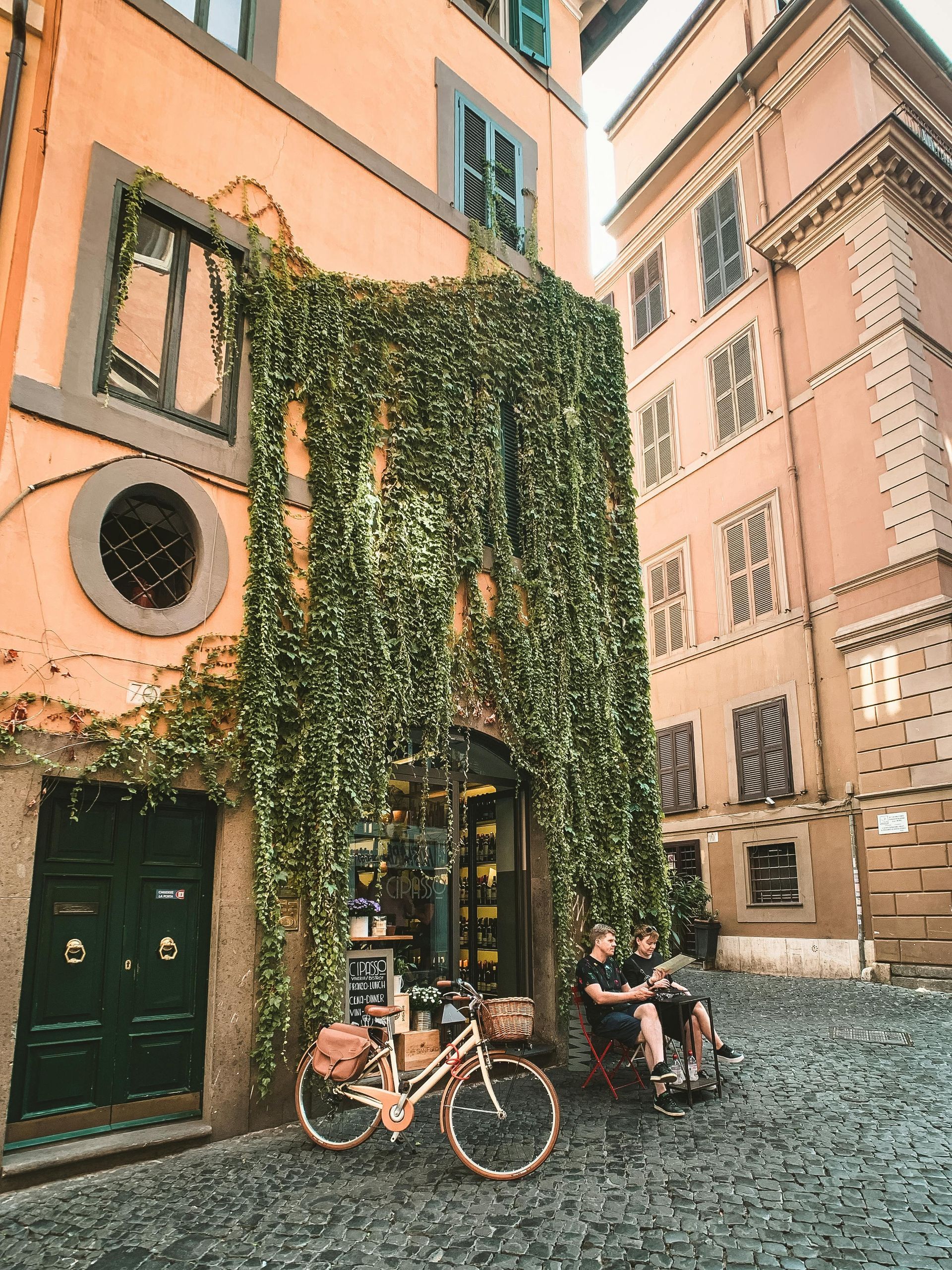 A bicycle is parked in front of a building with ivy growing on it in Rome, Italy.