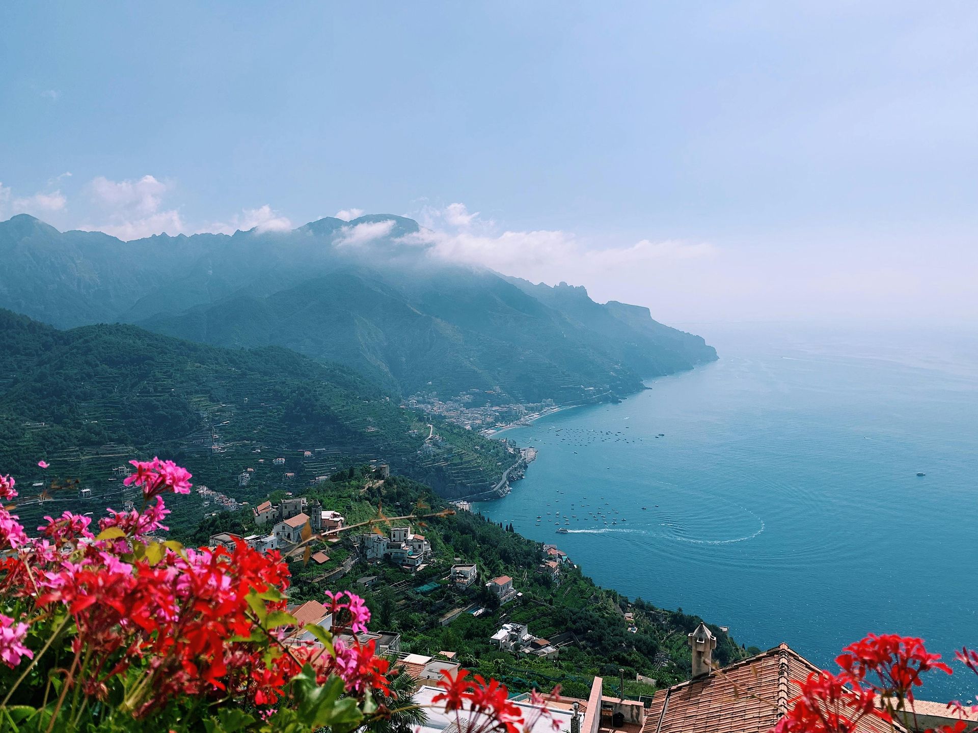 A view of a body of water with mountains in the background and flowers in the foreground in the Amalfi Coast, Italy