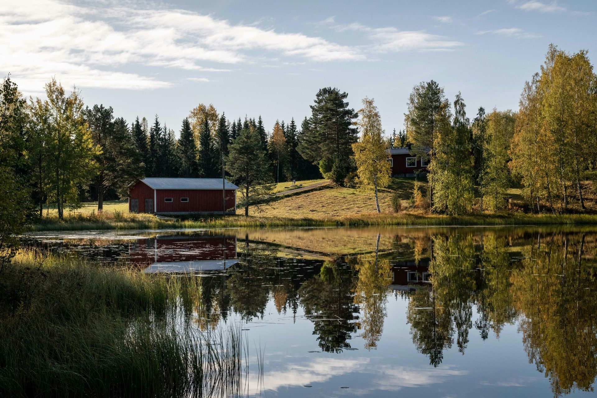 A red barn is sitting on the shore of a lake surrounded by trees in Finland.