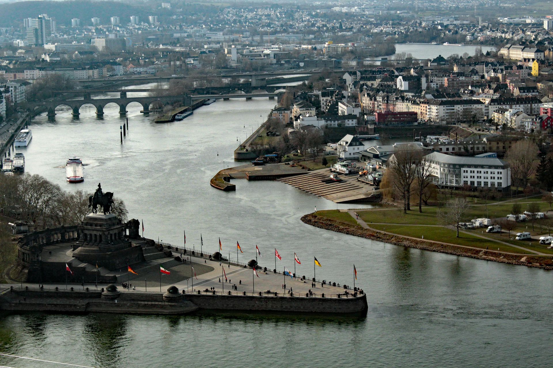 View of Koblenz, Germany, where the Moselle River meets the Rhine River, featuring a monument, bridges, and buildings.