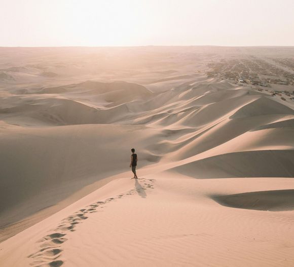A person is walking up a sand dune in the desert.