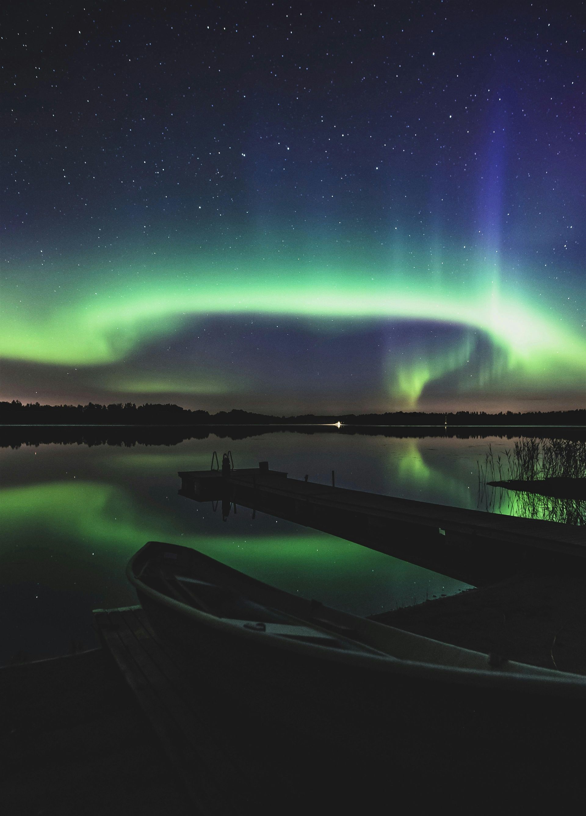 The aurora borealis is visible over a lake at night in Finland.