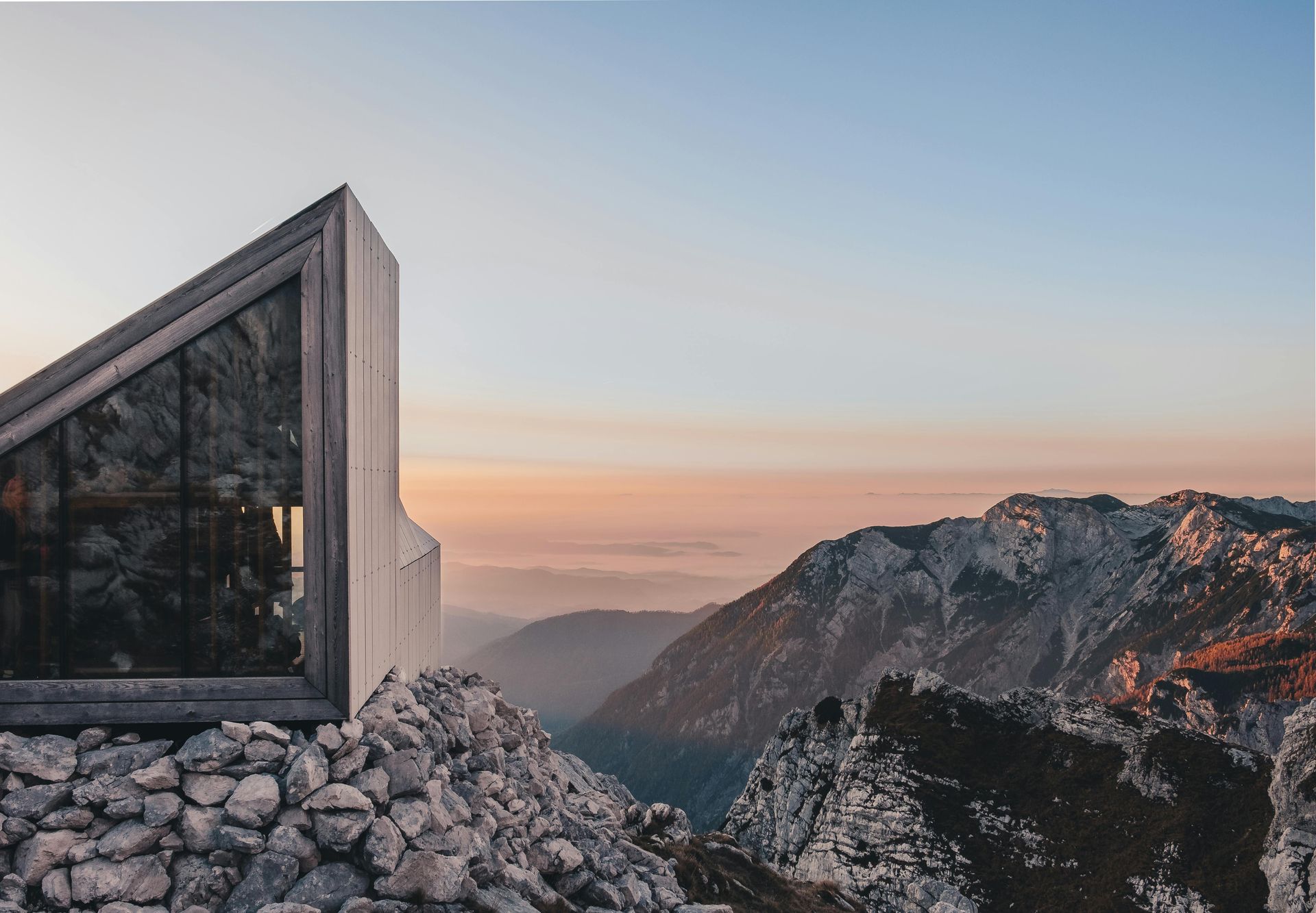 A house sits on top of a rocky mountain overlooking the Balkan mountains in Slovenia. 