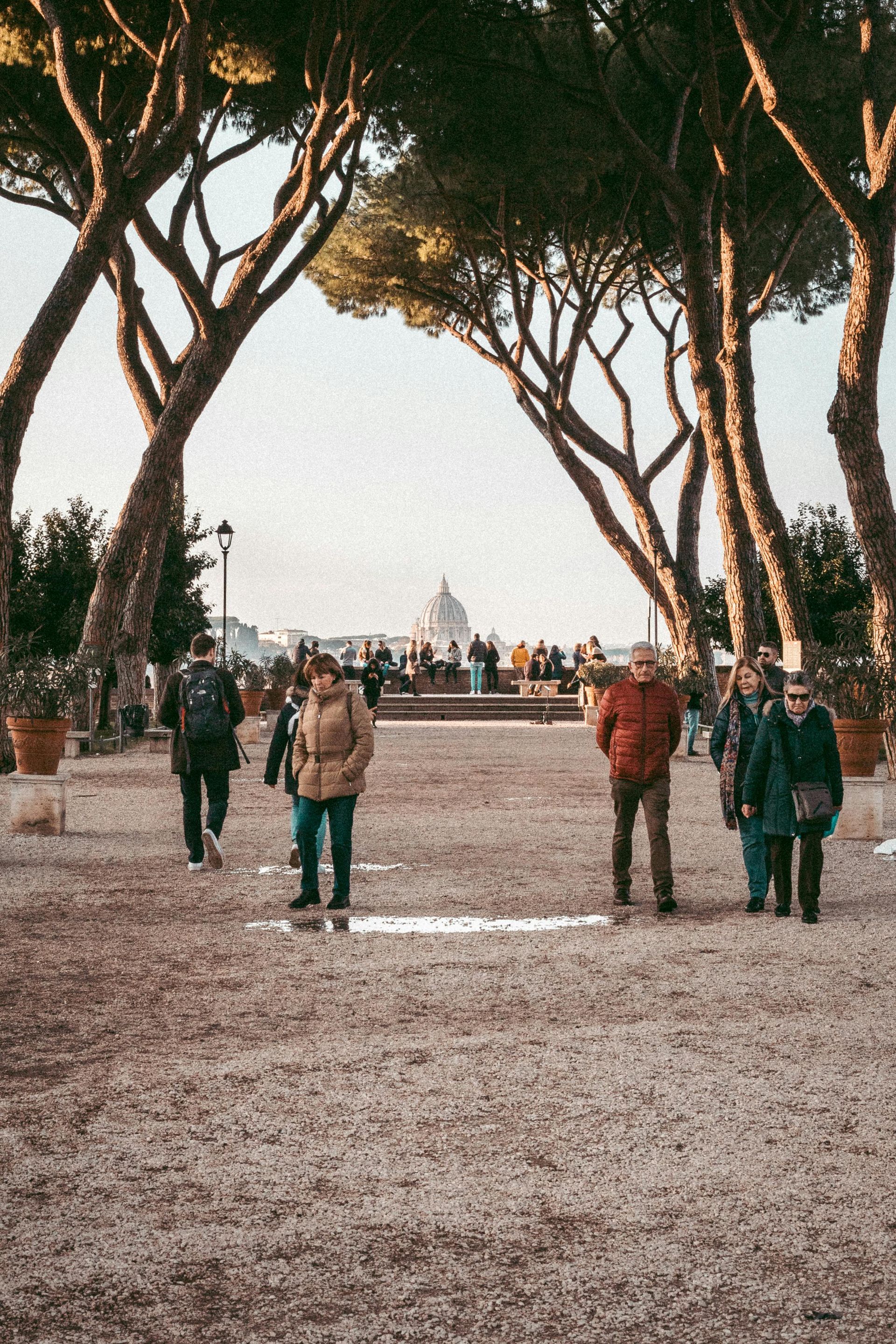 A group of people are walking down a dirt road surrounded by trees in Rome, Italy.