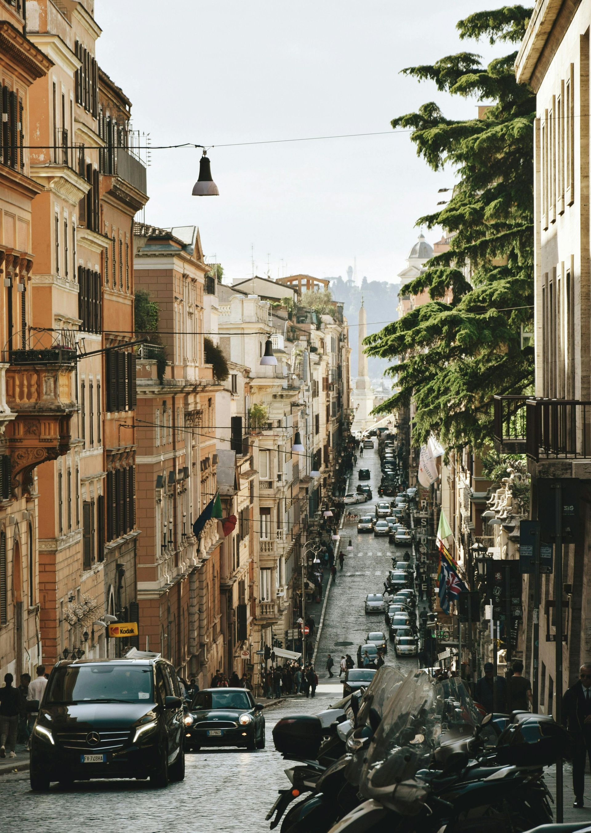 A narrow street with a lot of cars and motorcycles on it in Rome, Italy.