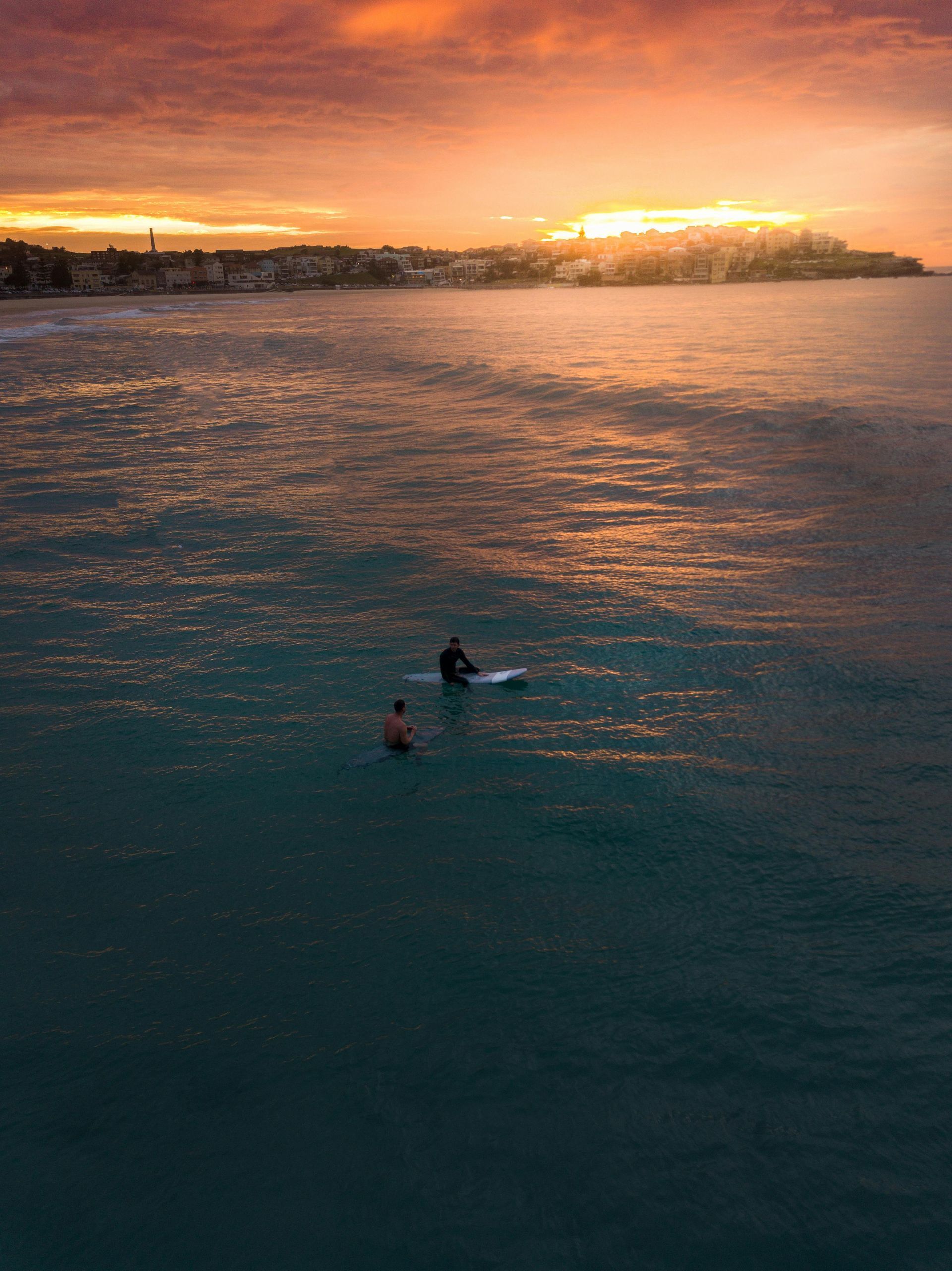 A couple of people are surfing in the ocean at sunset in Australia.