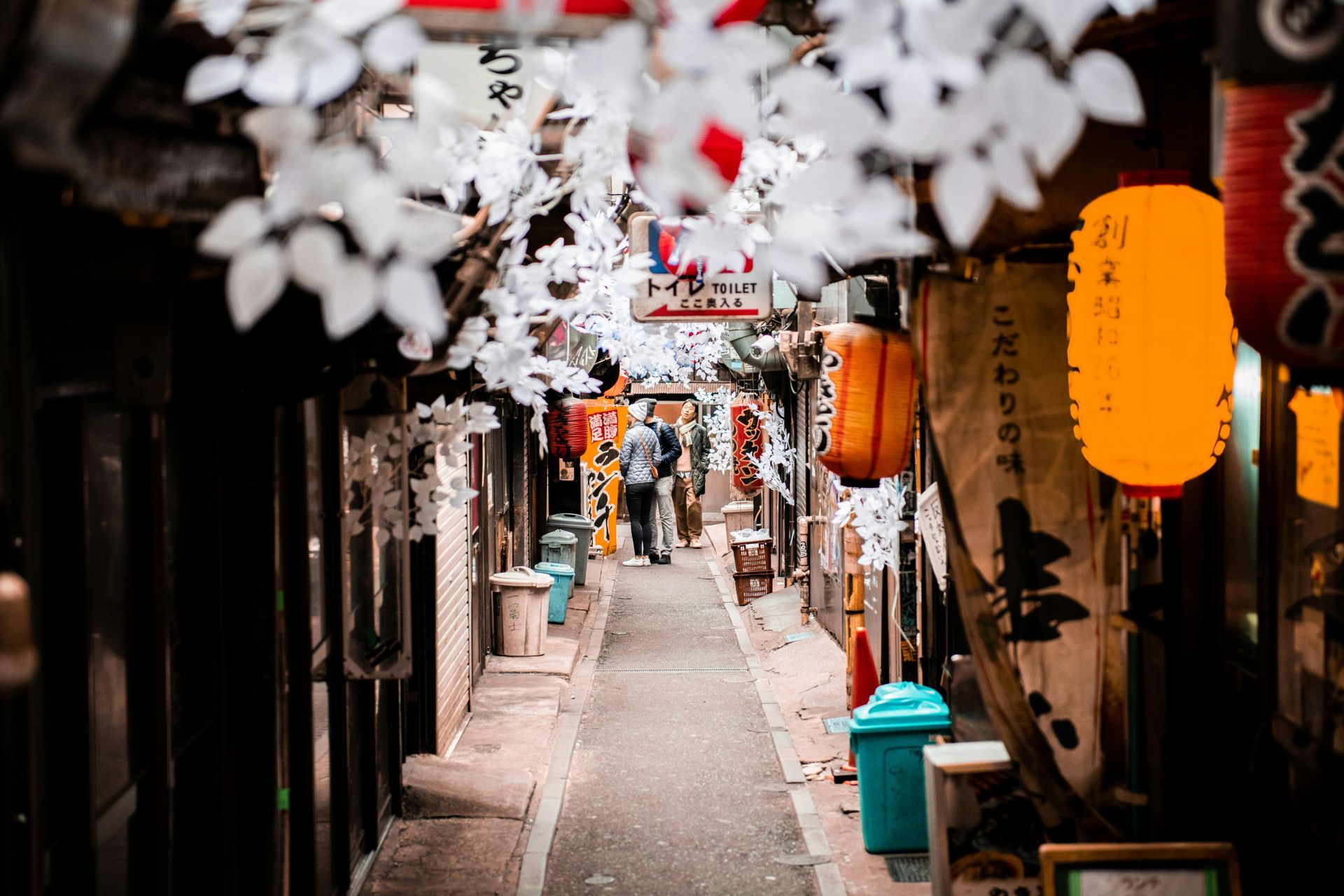 A narrow alleyway filled with lots of shops, lanterns, and cherry blossoms in Japan.