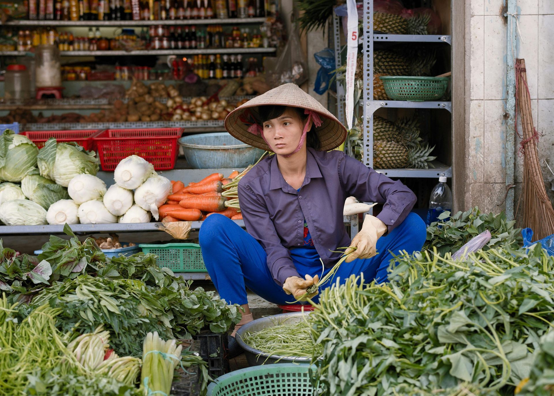 A woman is sitting on the ground selling vegetables at a market in Vietnam.