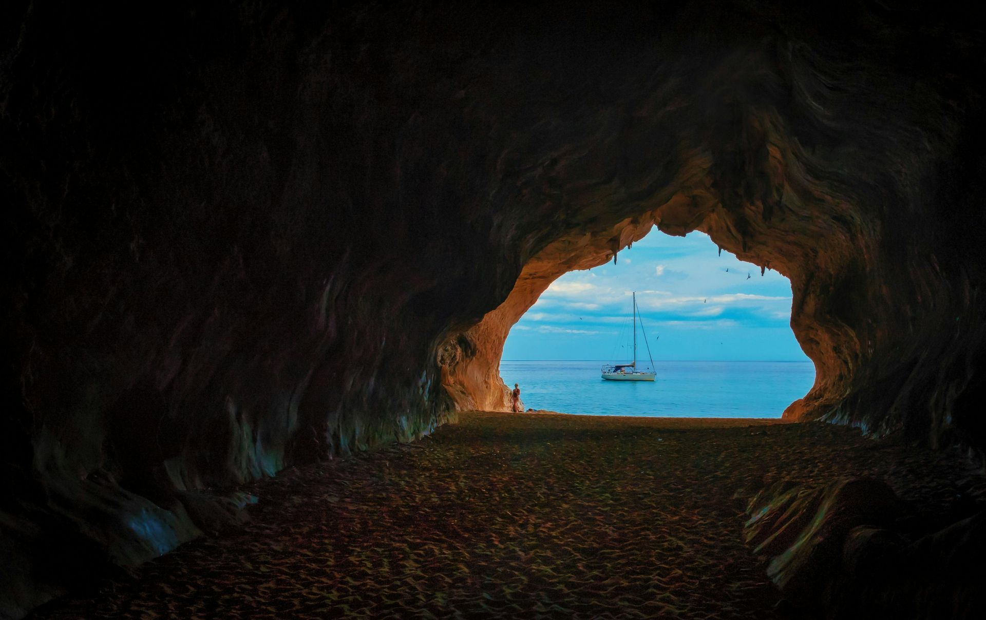 A cave with a view of the mediterranean ocean and a boat in the water.