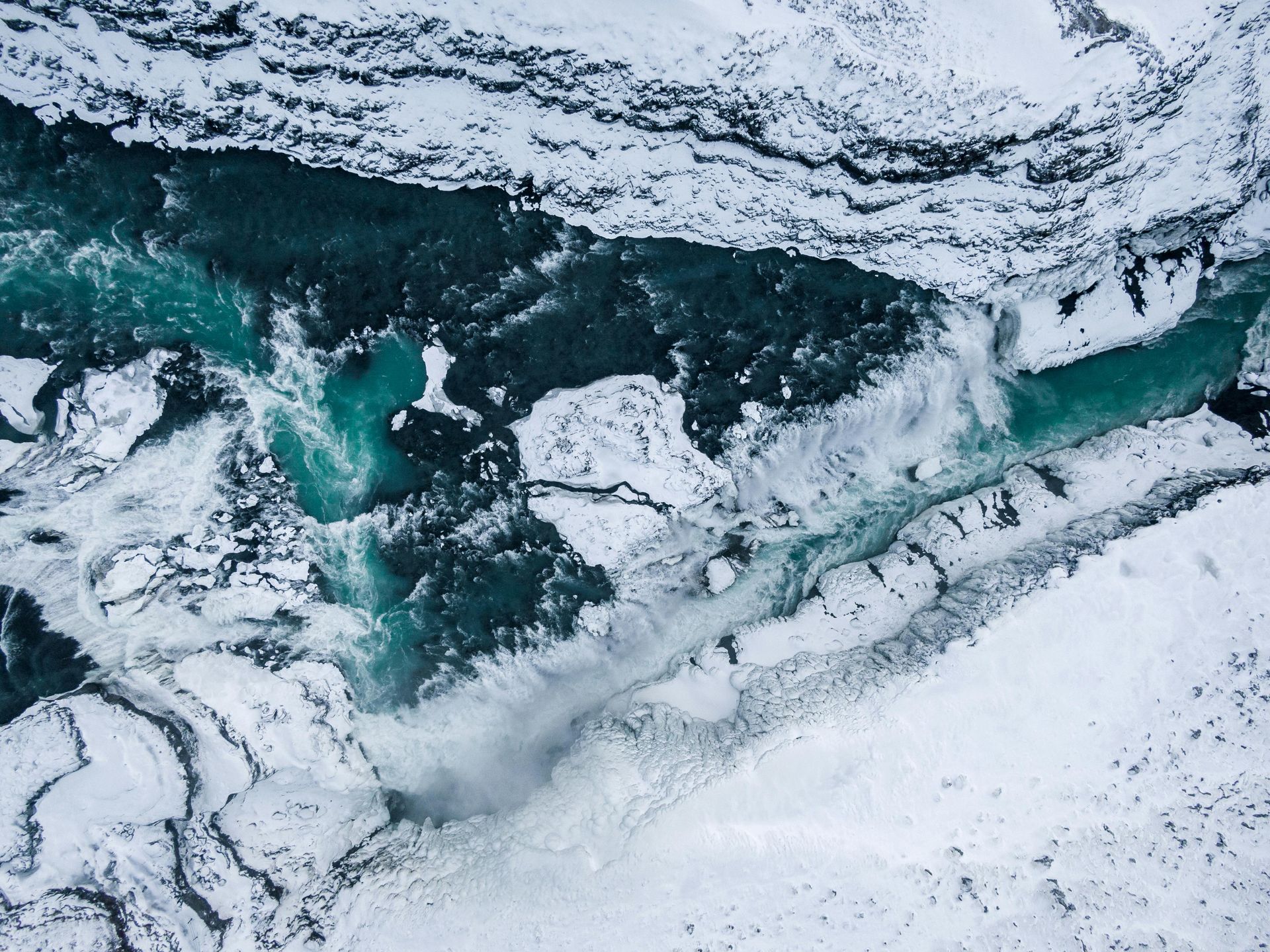 An aerial view of a river flowing through a snowy landscape in Iceland.