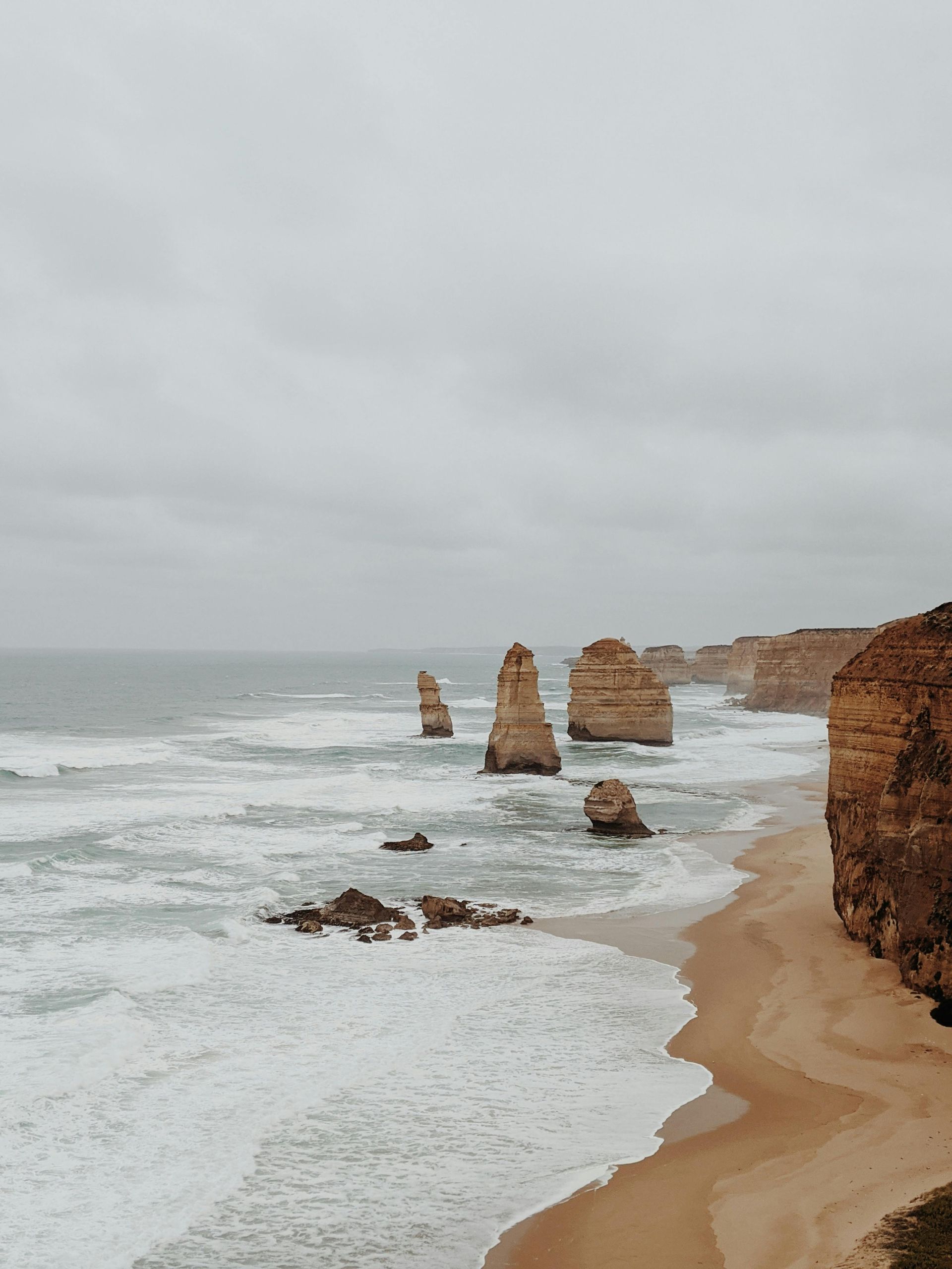 A beach with rocks in the water and a cliff in the background in Australia.