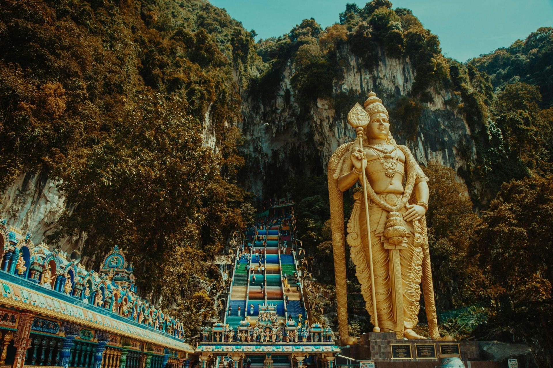 Golden Buddha statue at the Batu caves in front of a staircase leading to a temple in Malaysia.