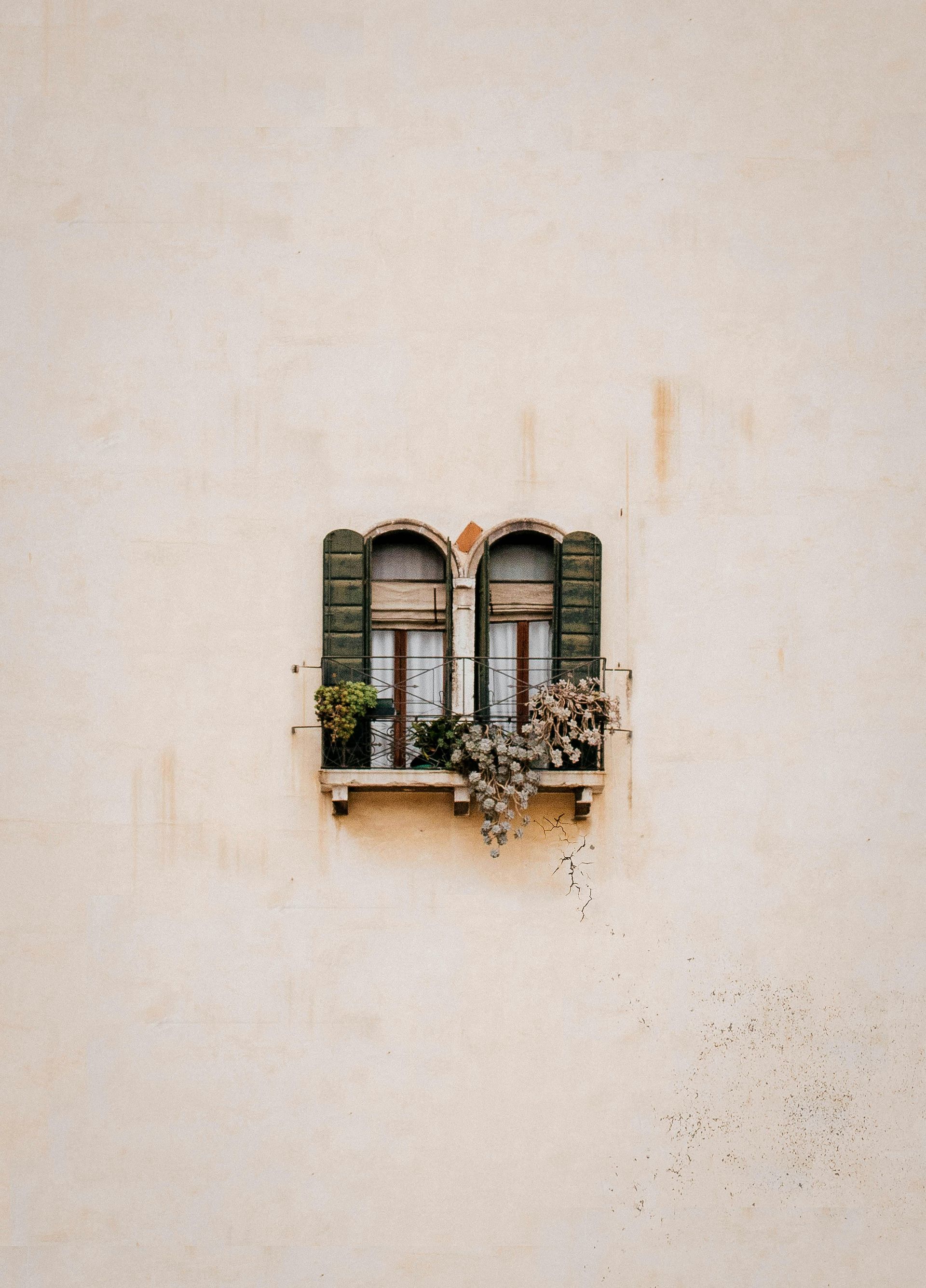 A window with green shutters on a white wall in Venice, Italy.