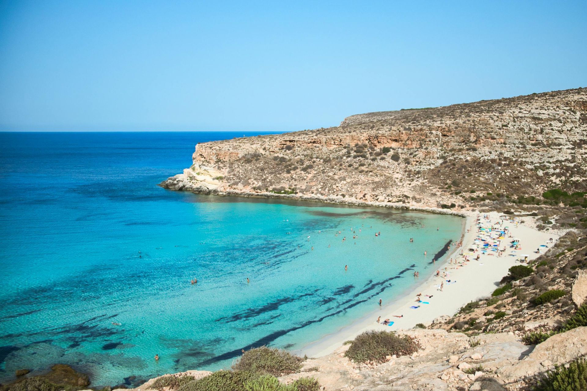 A beach with a lot of people swimming in the water in Sicily, Italy.