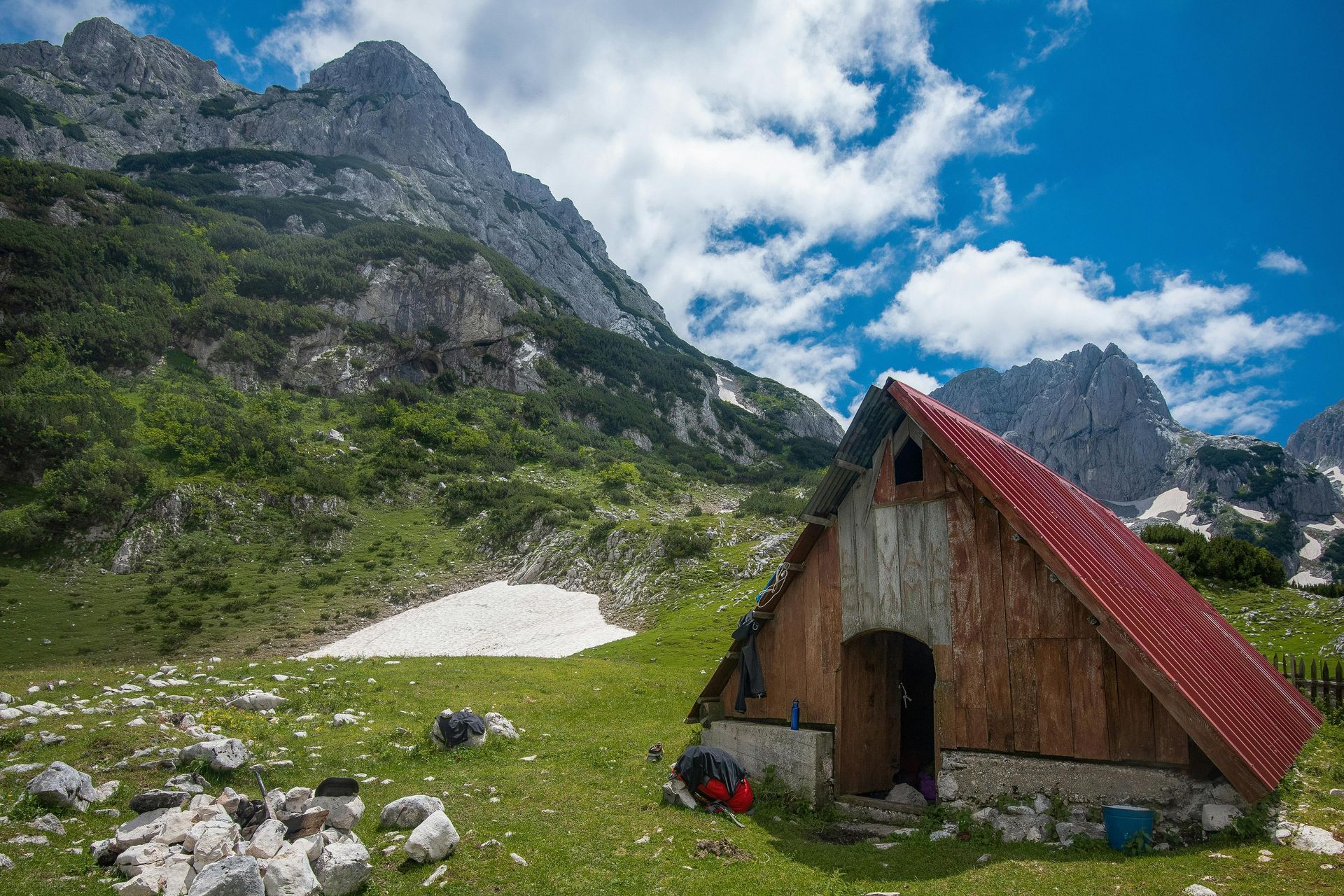 A small wooden hut with a red roof in the middle of a grassy field in the mountains at Durmitor National Park in Montenegro. 